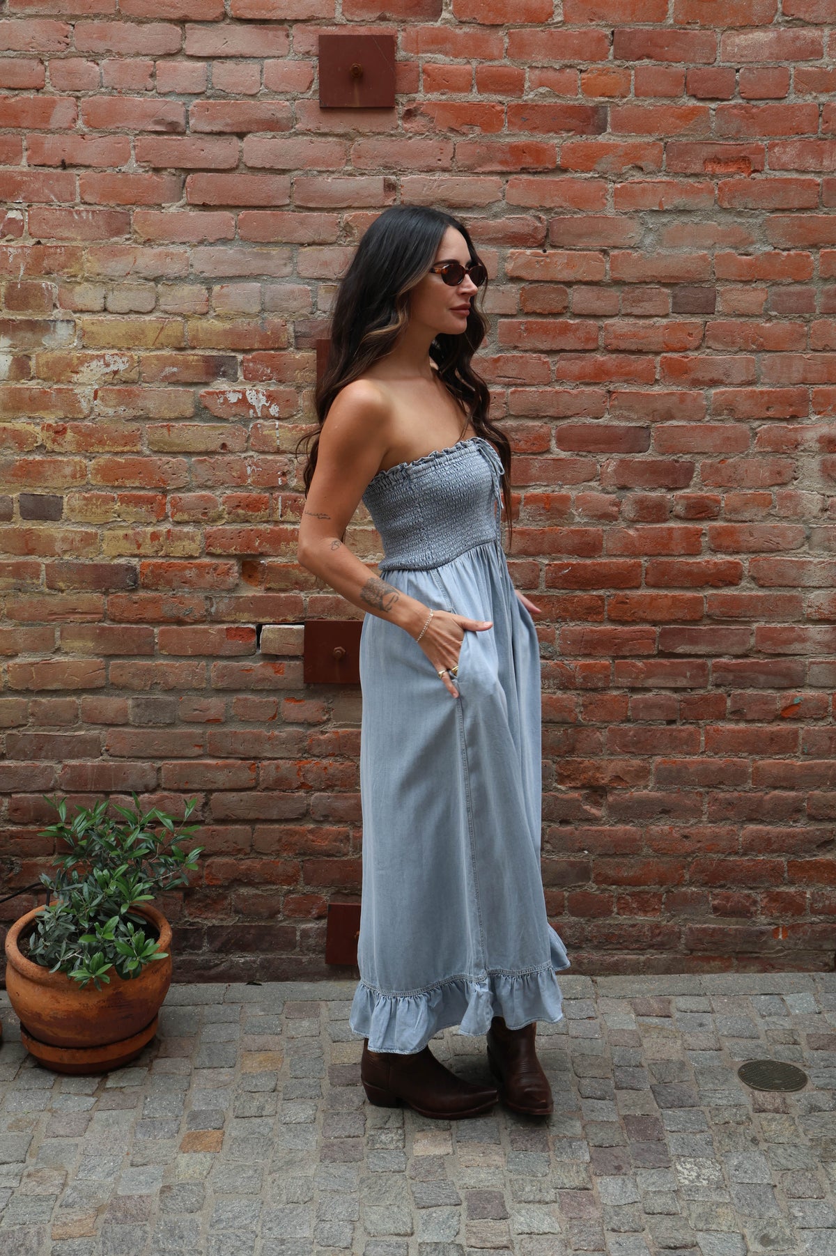 Woman in a strapless light blue dress standing against a brick wall.