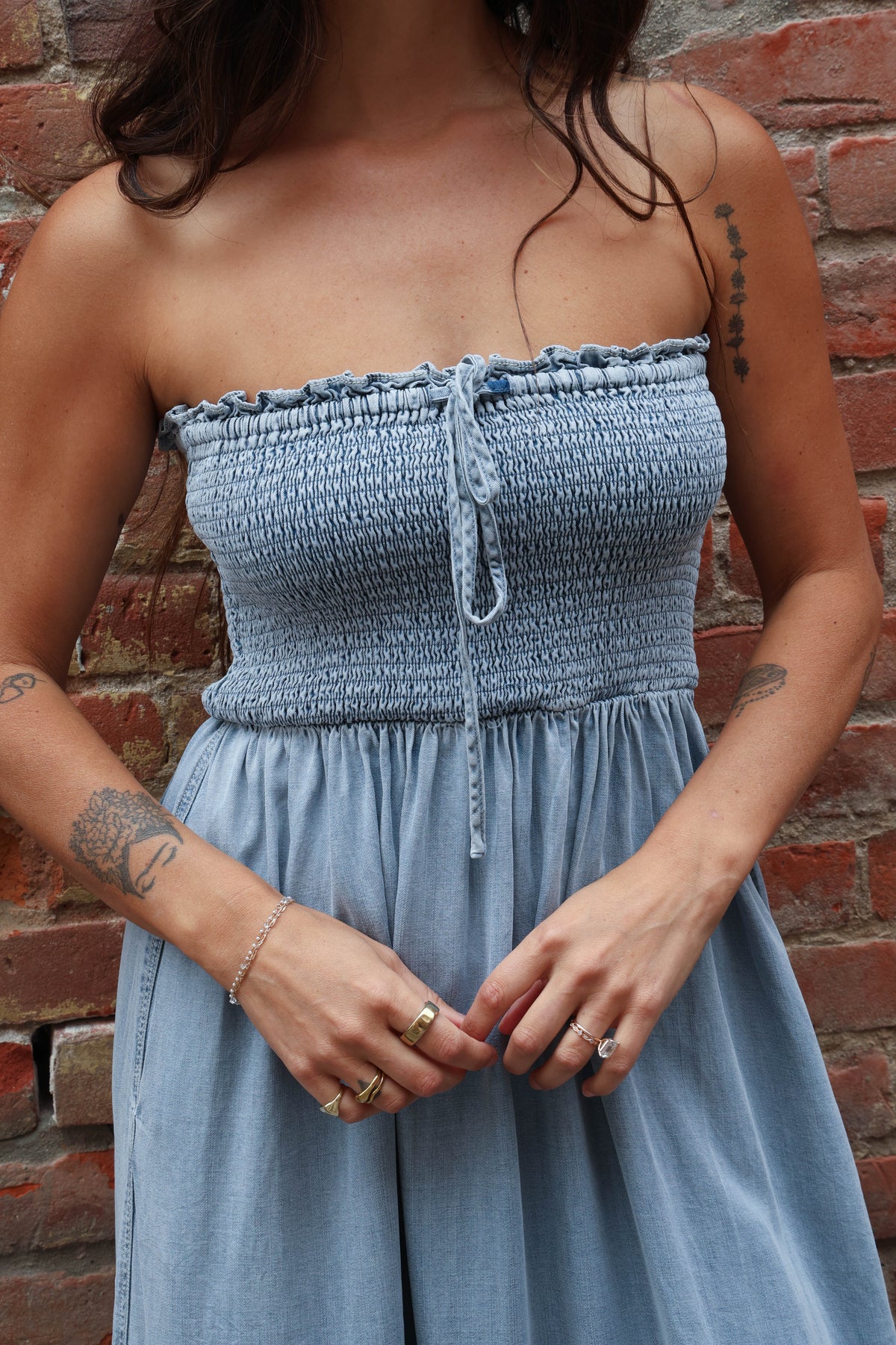 Woman wearing a light blue strapless dress against a brick wall.