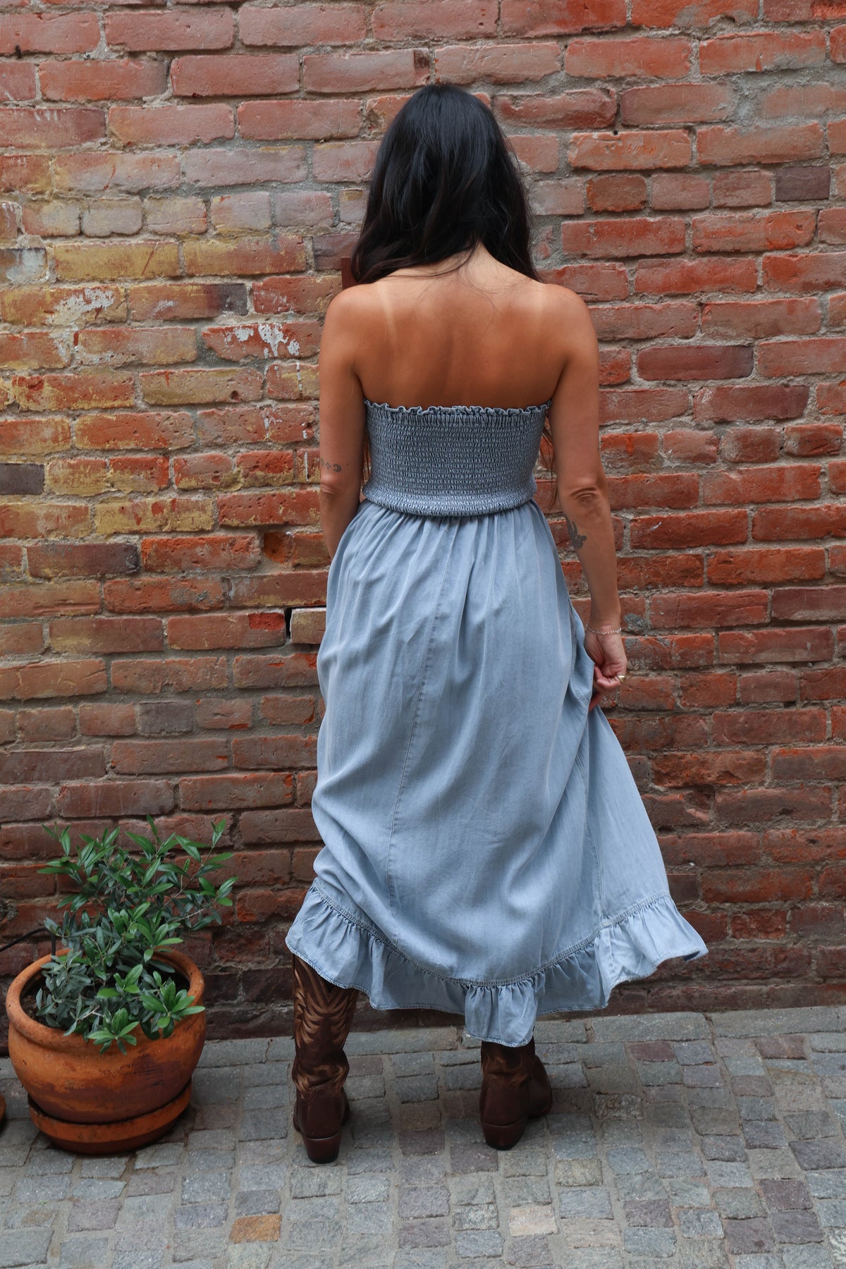 Woman in a strapless dress and boots standing against a brick wall.