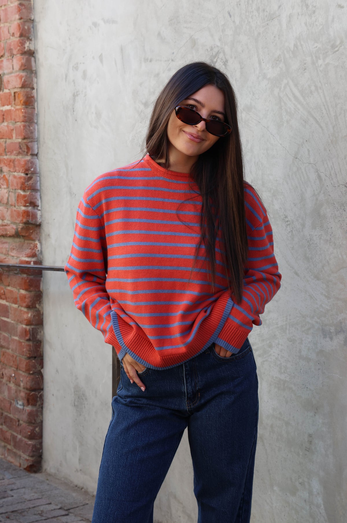 Woman wearing a striped sweater with jeans standing against a plain wall.