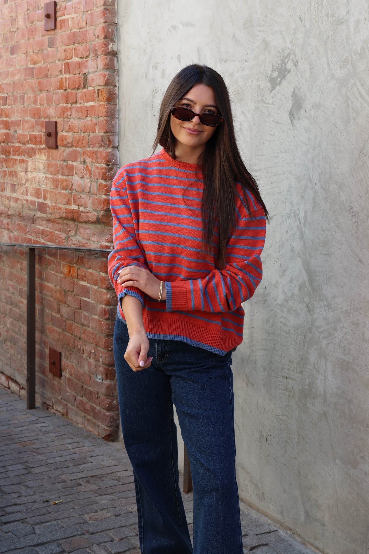 Woman wearing a striped sweater with jeans standing against a plain wall.