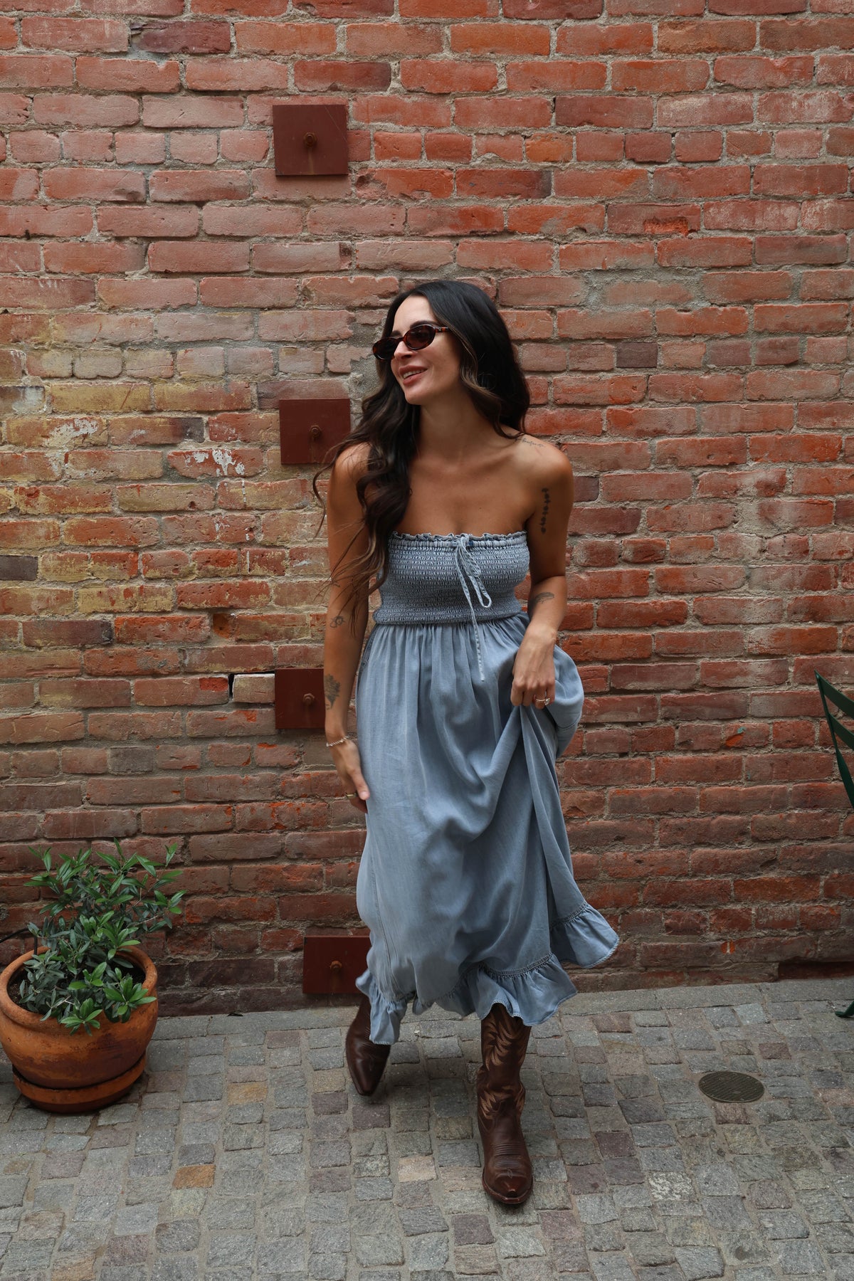 Woman in a strapless dress and boots standing against a brick wall.