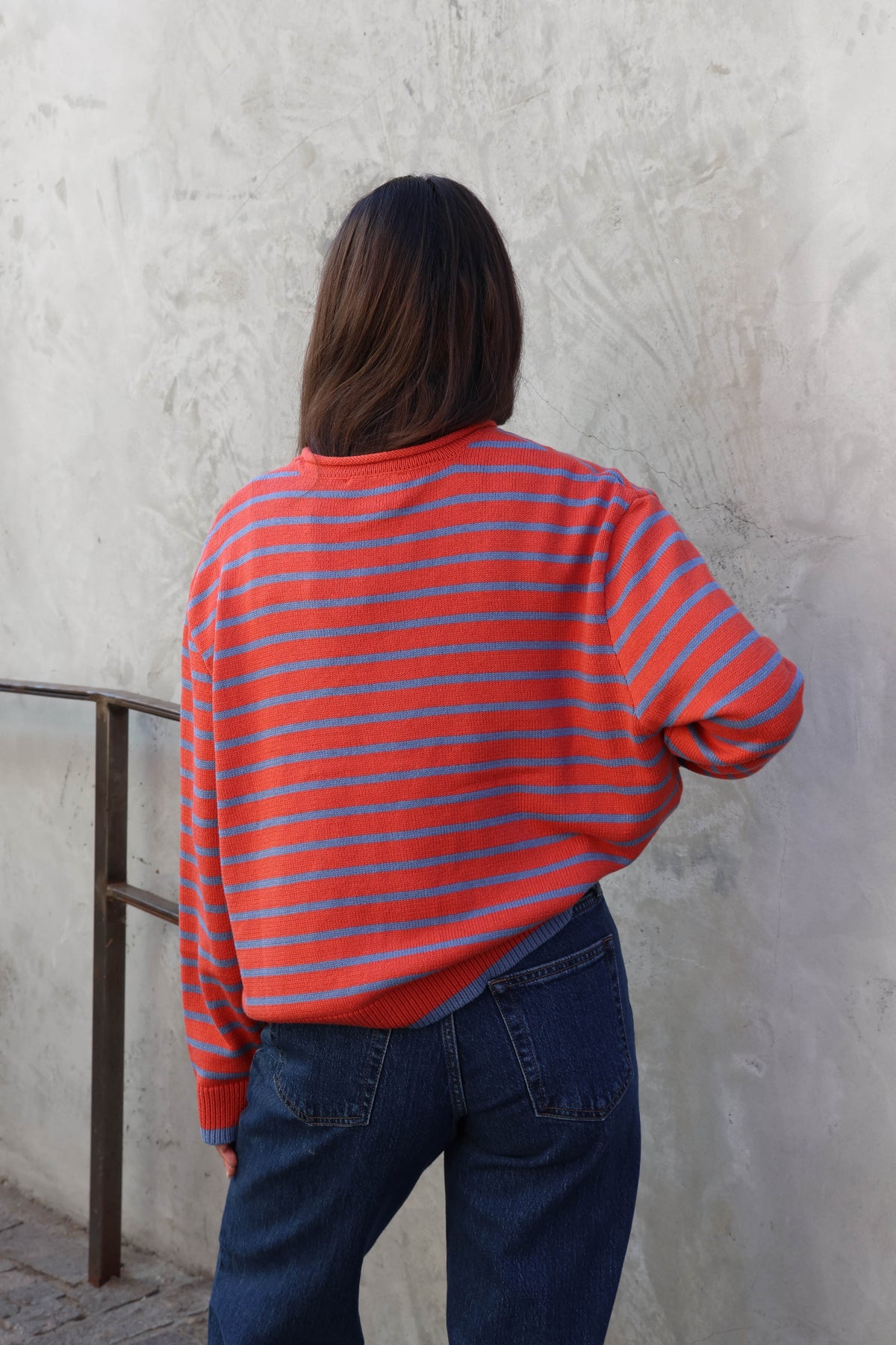 Woman wearing a striped sweater with jeans standing against a plain wall.