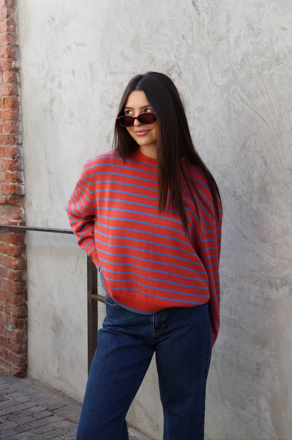Woman wearing a striped sweater with jeans standing against a plain wall.