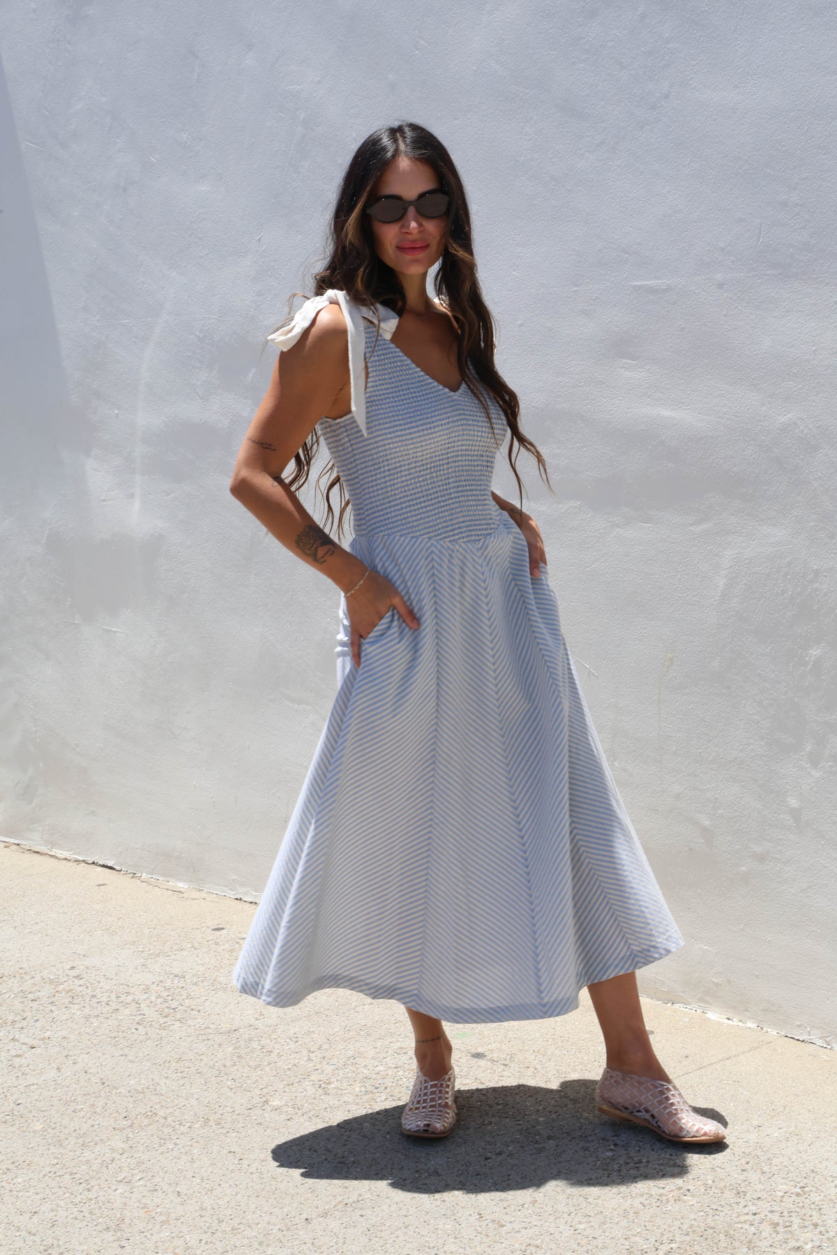 Woman wearing a gingham dress with ties against a white wall
