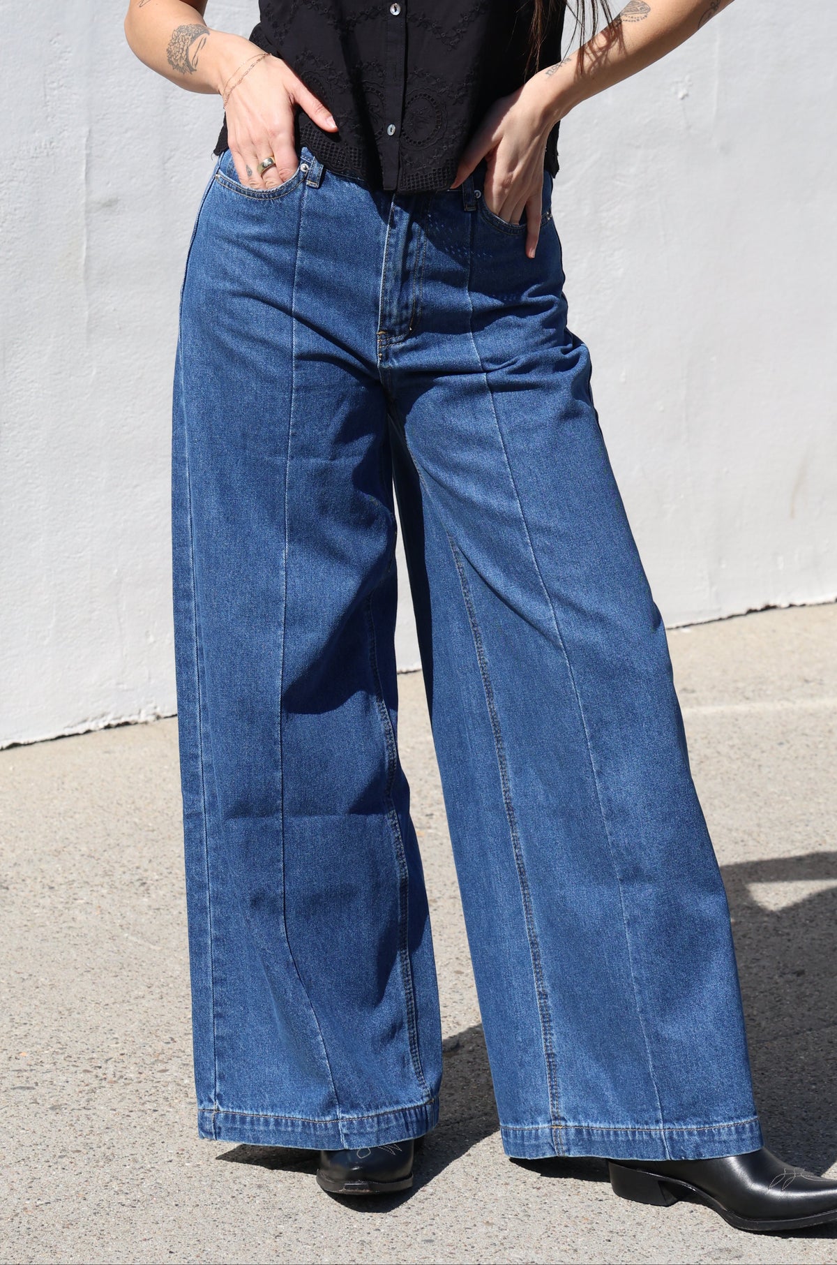 Woman wearing blue jeans and a black top on a light gray pavement.