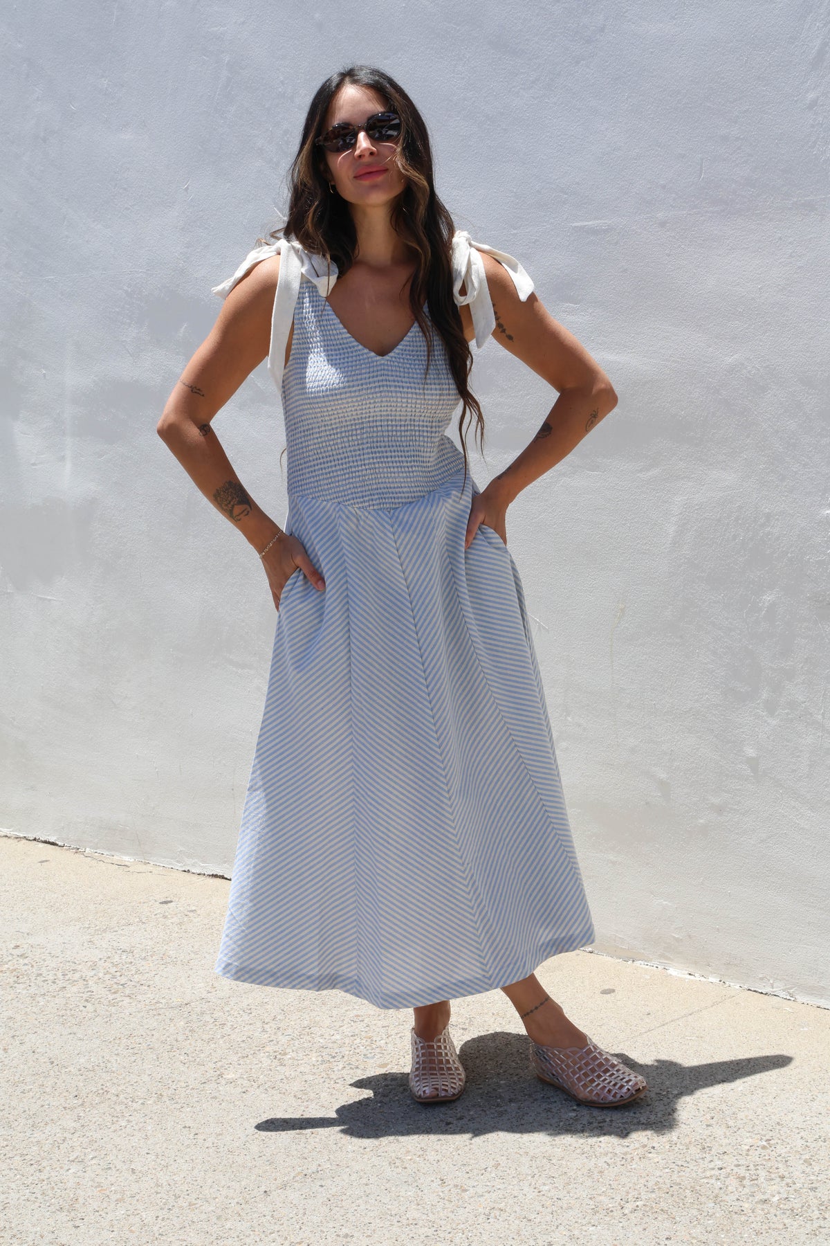 Woman wearing a gingham dress with ties against a white wall