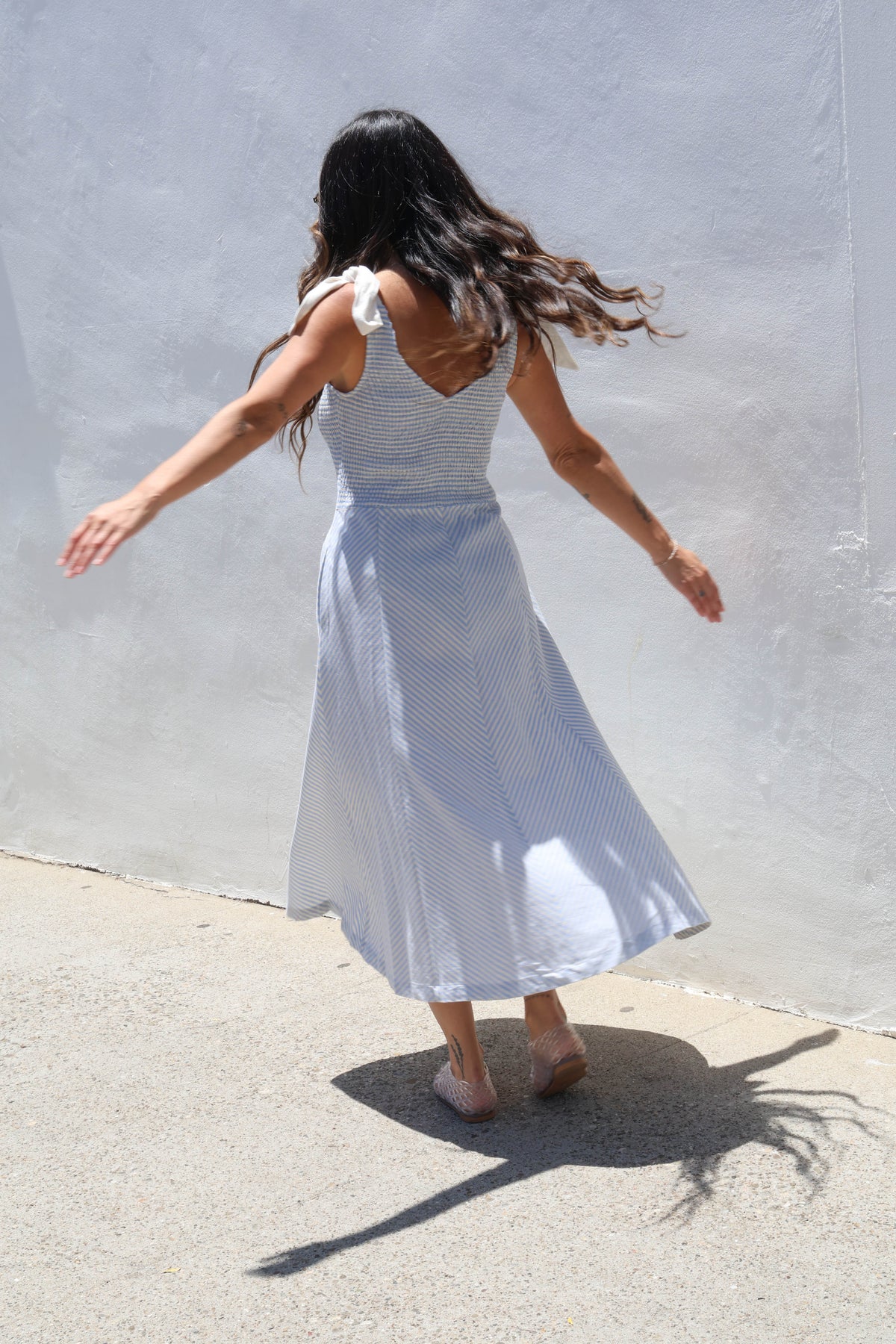 Woman wearing a gingham dress with ties against a white wall