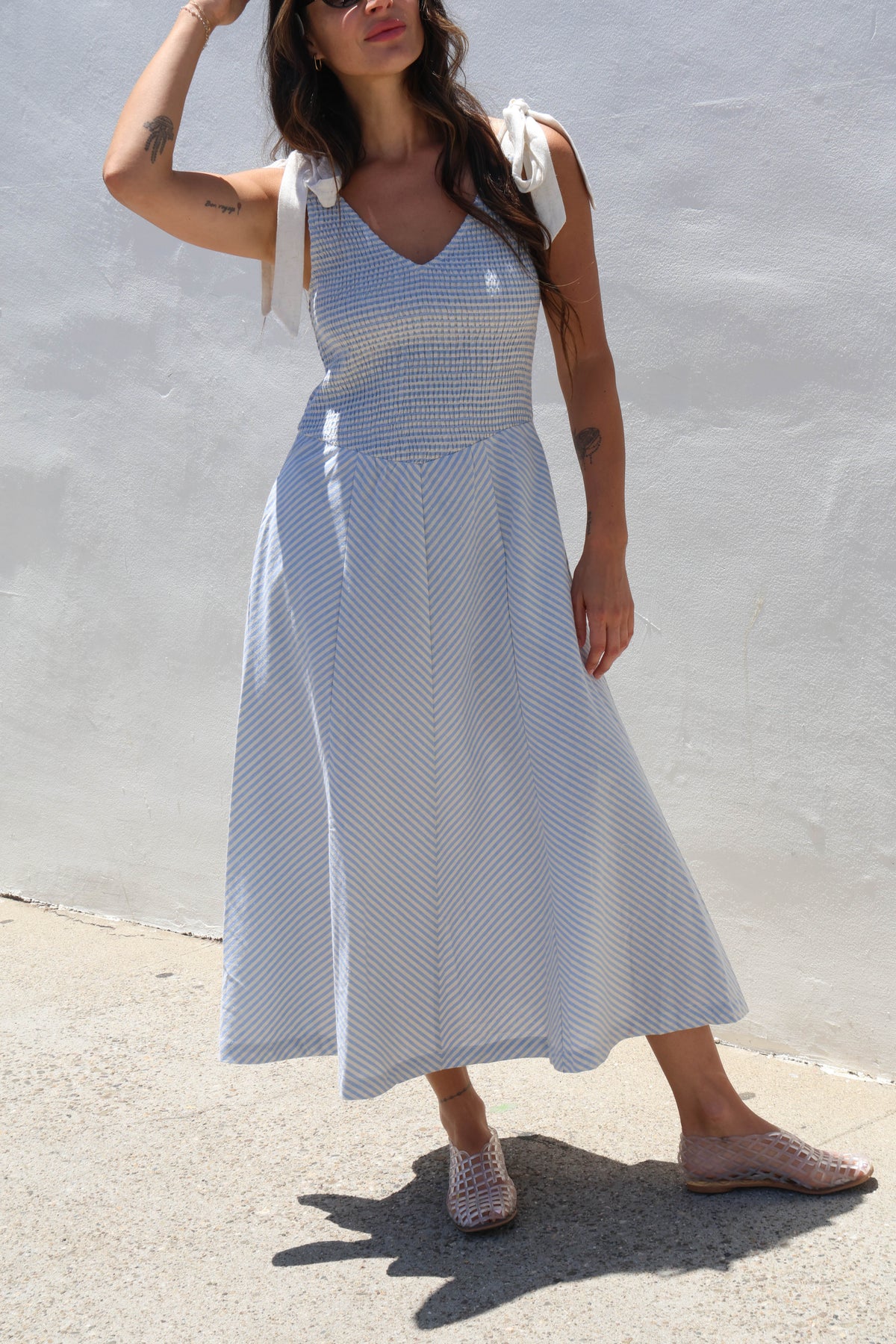 Woman wearing a blue and white patterned dress against a light gray wall.