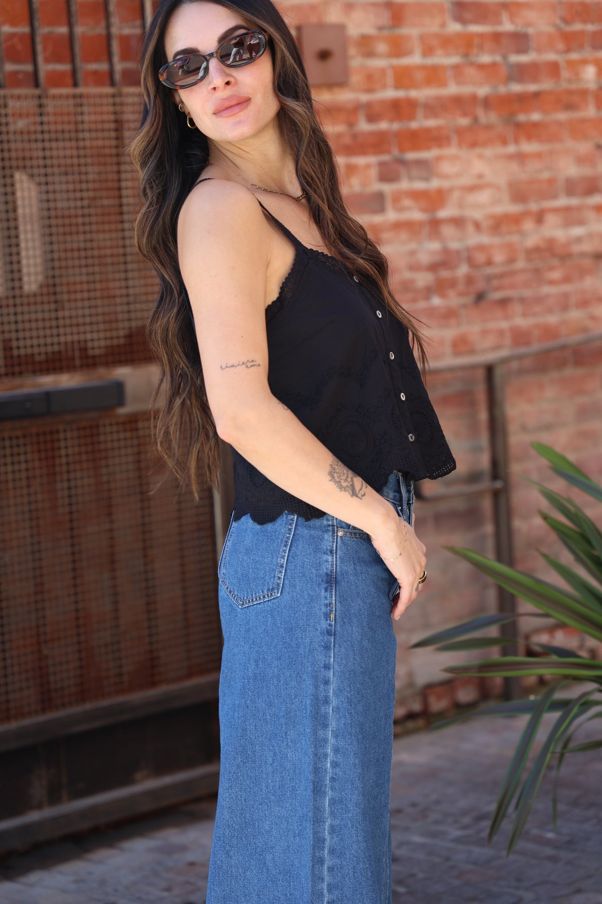 Woman wearing sunglasses and a black top with a brick wall background