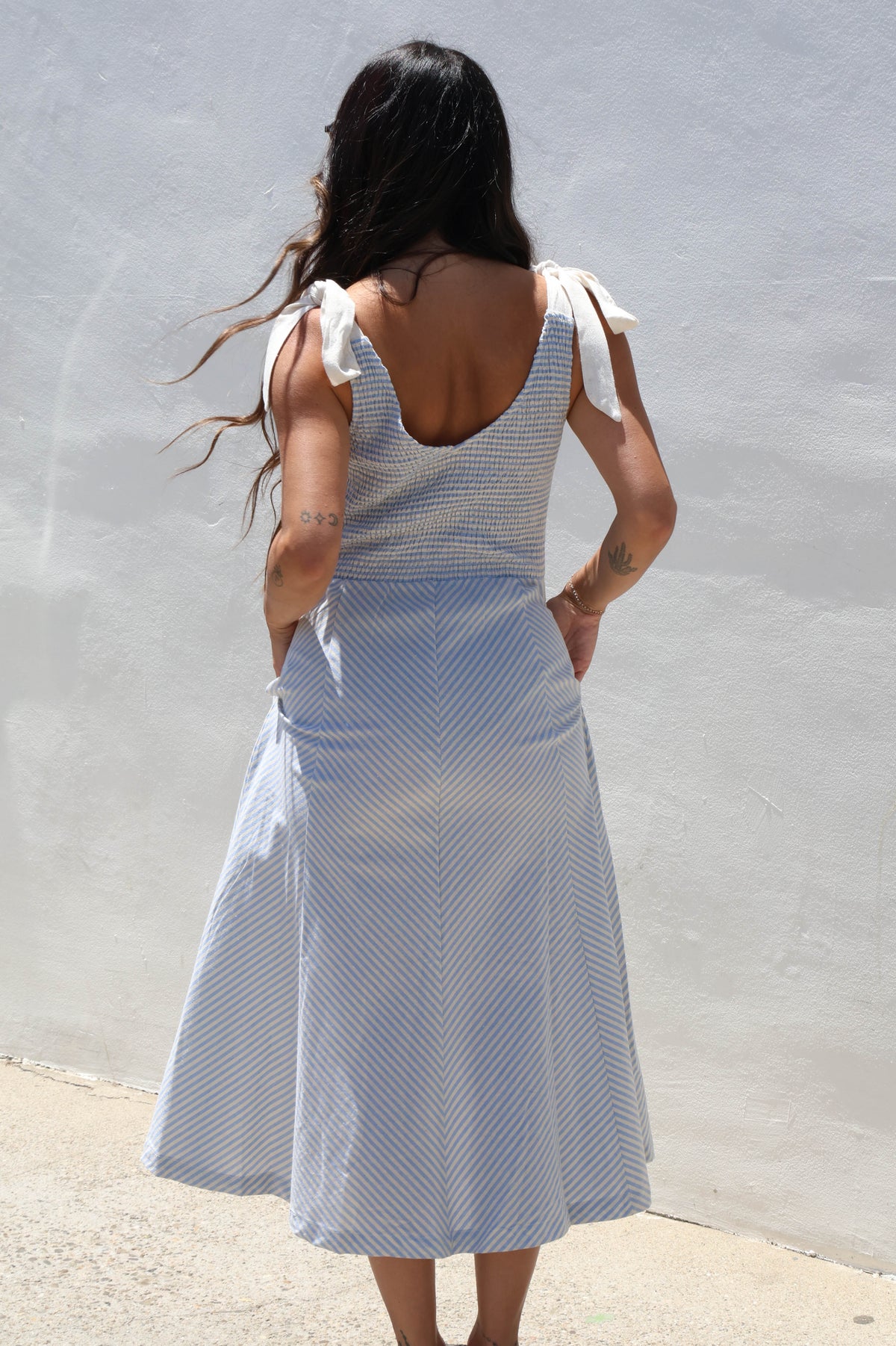 Woman wearing a gingham dress with ties against a white wall