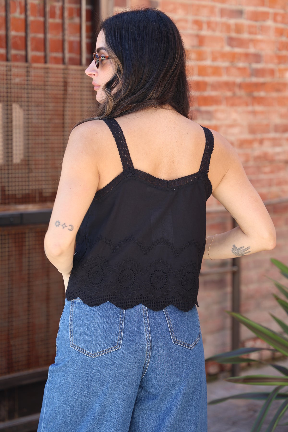 Woman wearing a black sleeveless top and blue jeans against a brick wall.