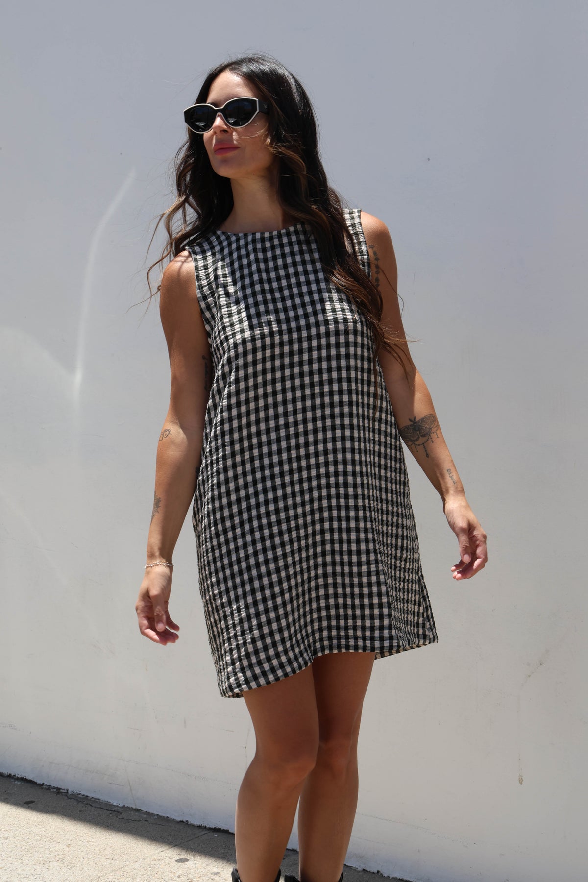 Woman wearing a black and white checkered dress against a white wall.