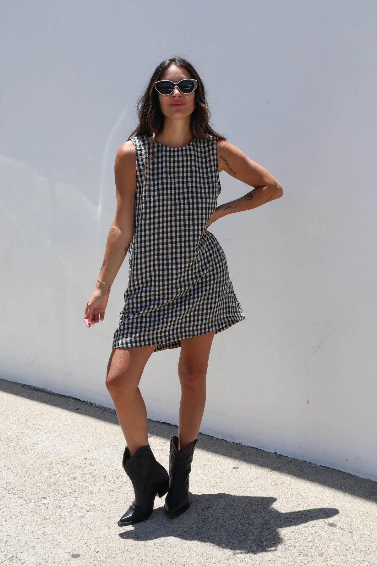 Woman wearing a black and white checkered dress with black boots against a white wall.