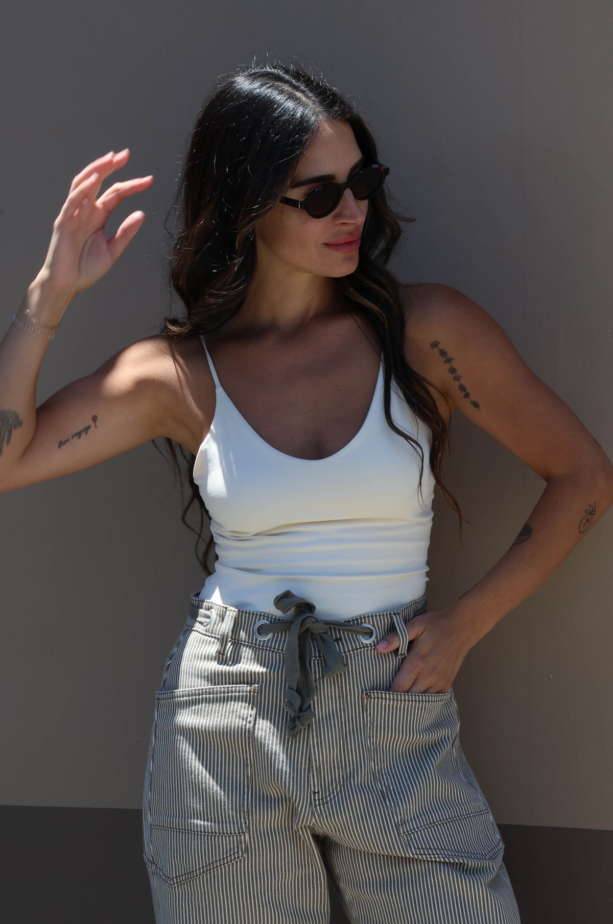 Woman wearing a white tank top and light-colored pants against a plain background