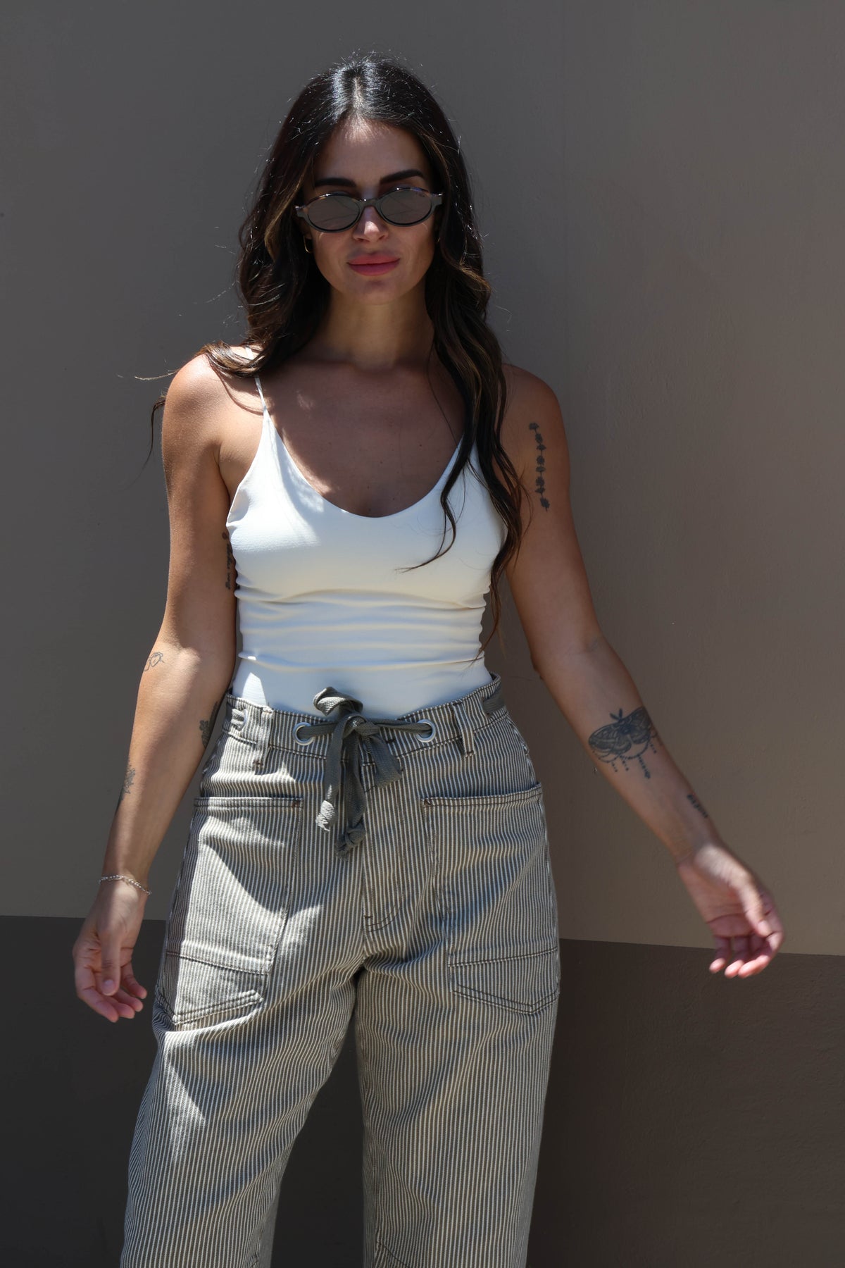 Woman wearing a white tank top and light-colored pants against a plain background