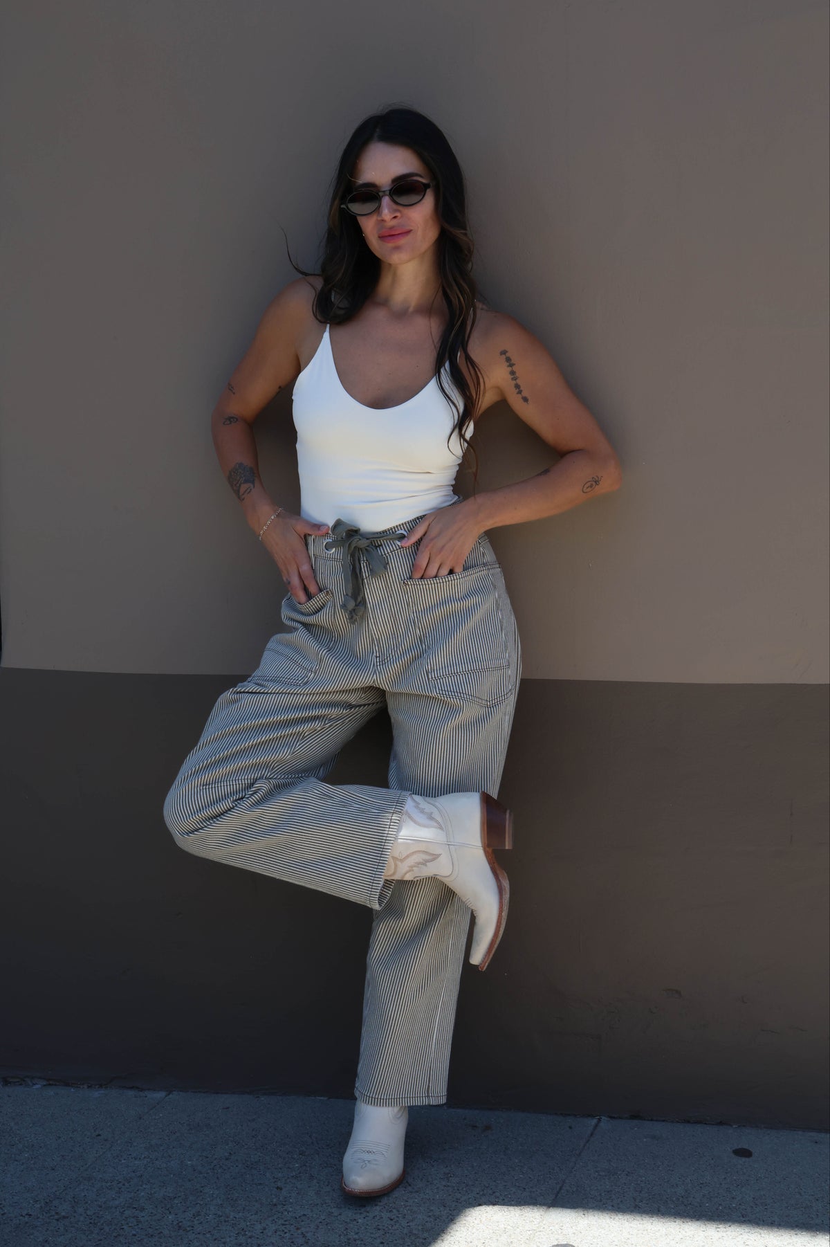 Woman posing against a wall wearing sunglasses and casual clothing.