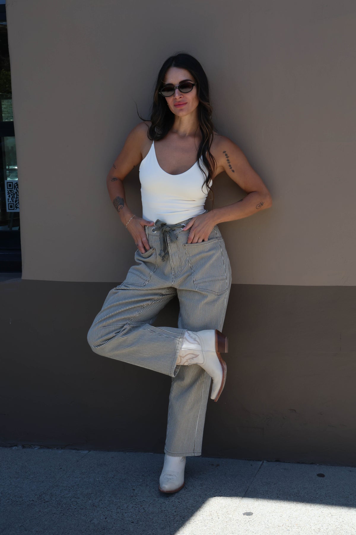 Woman wearing a white tank top and light-colored pants against a plain background