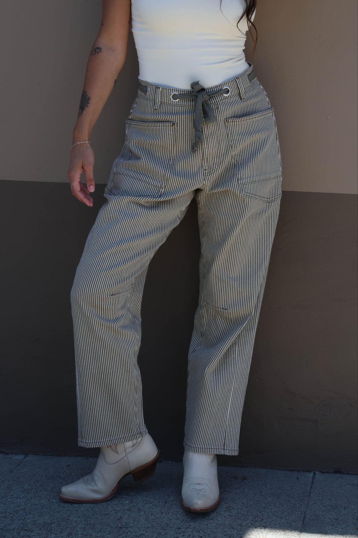 Person wearing a white tank top and high-waisted light blue jeans against a plain background