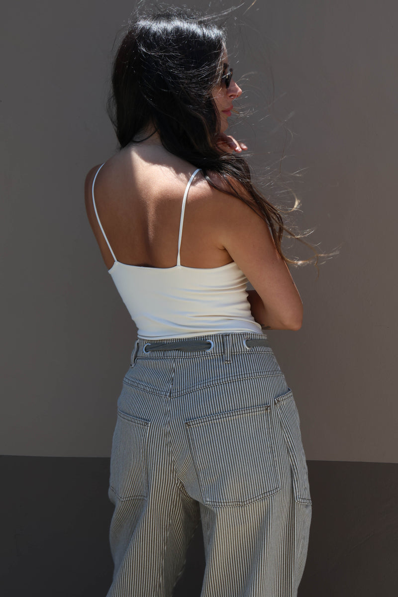 Woman wearing a white tank top and light-colored pants against a plain background