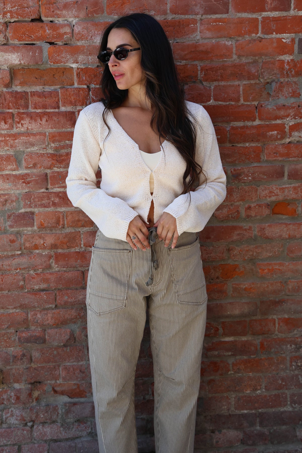 Woman wearing a white knit with striped pants against a brick wall