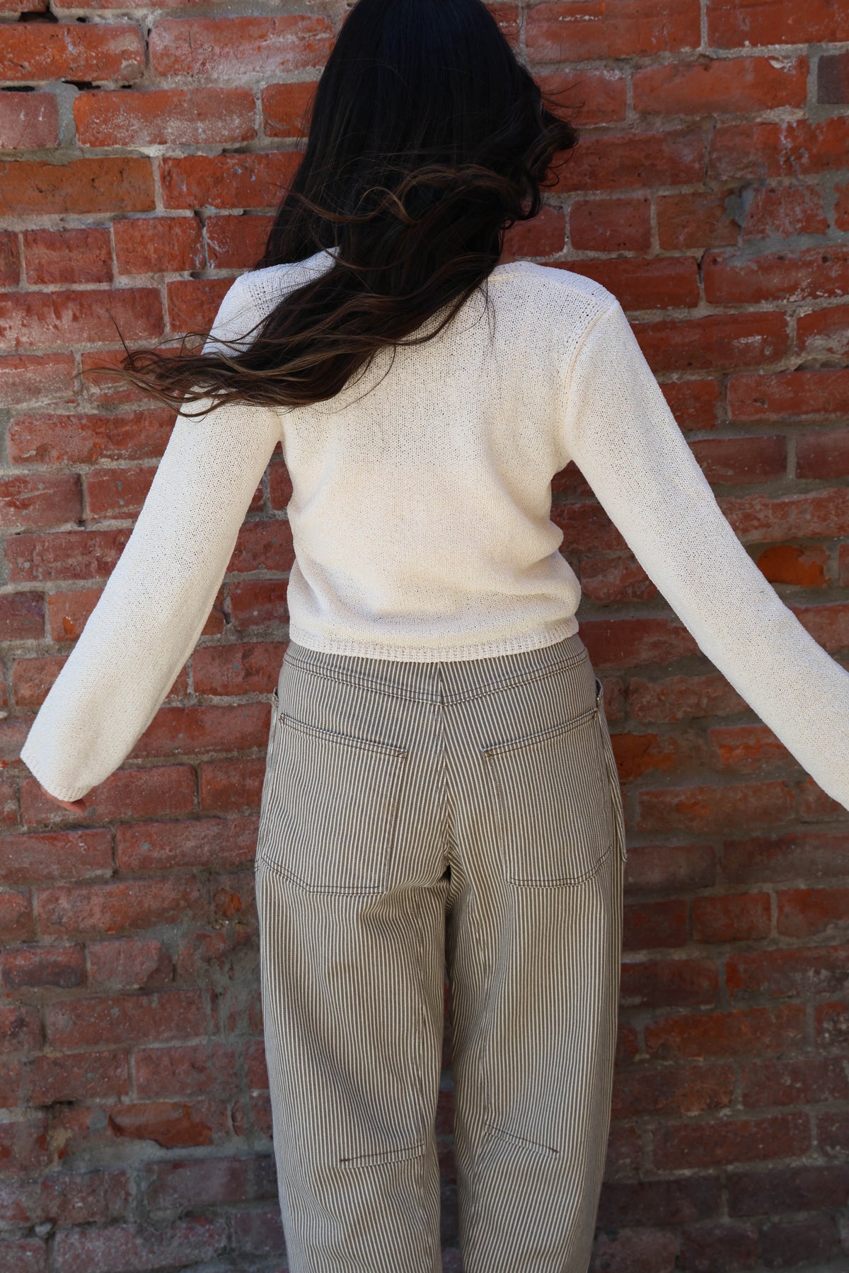 Woman wearing a white knit with striped pants against a brick wall