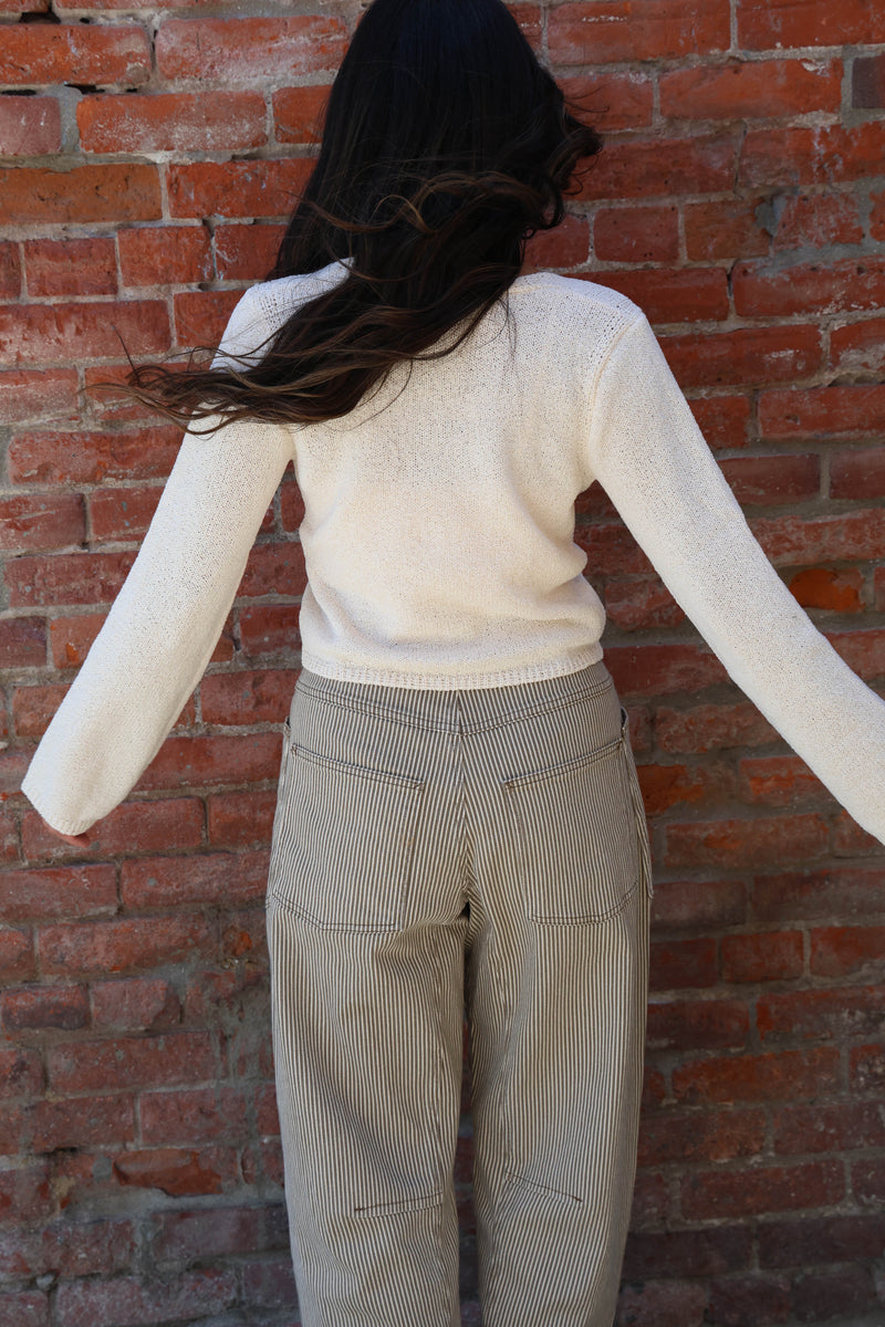Woman wearing a white knit with striped pants against a brick wall
