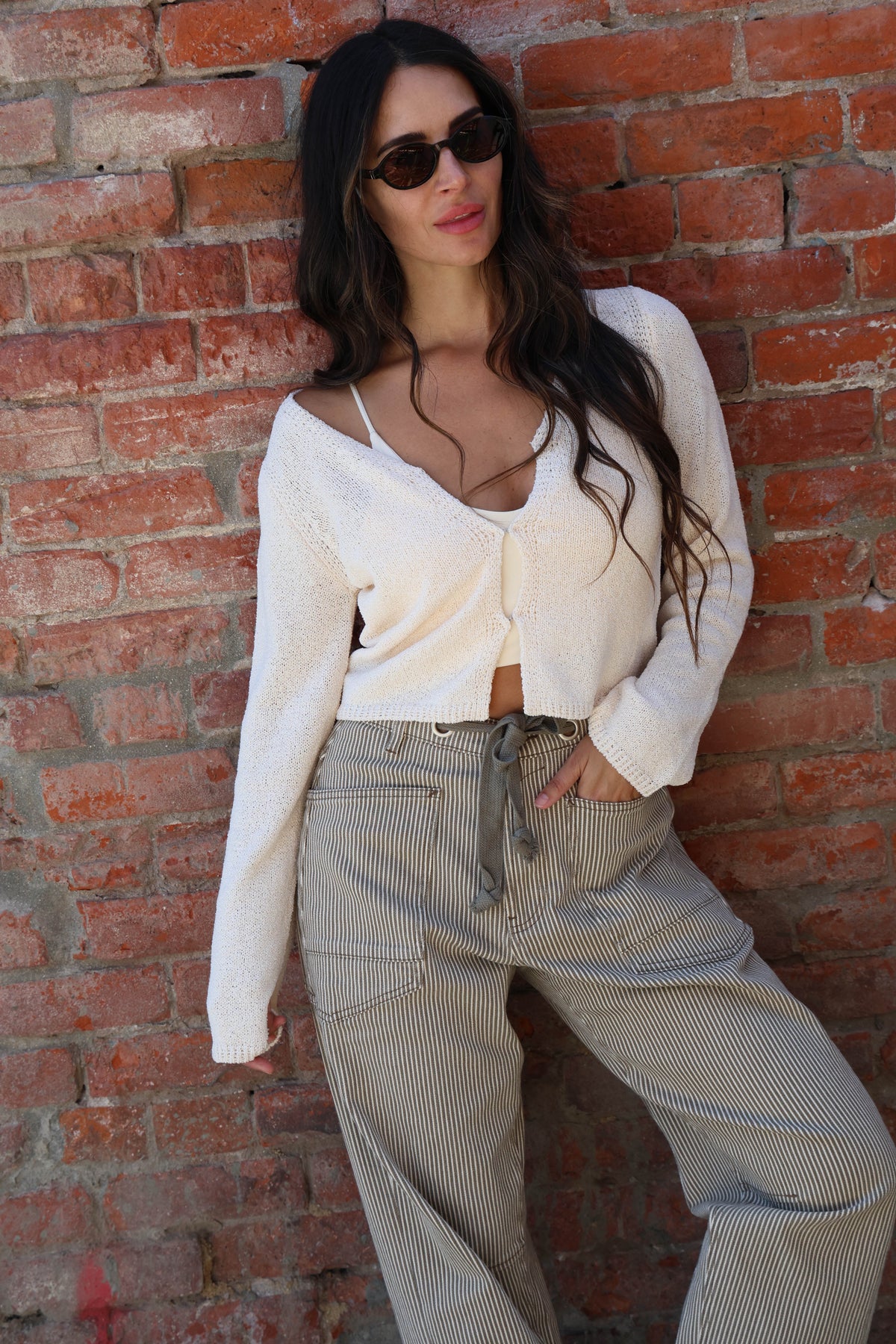 Woman wearing a white knit with striped pants against a brick wall