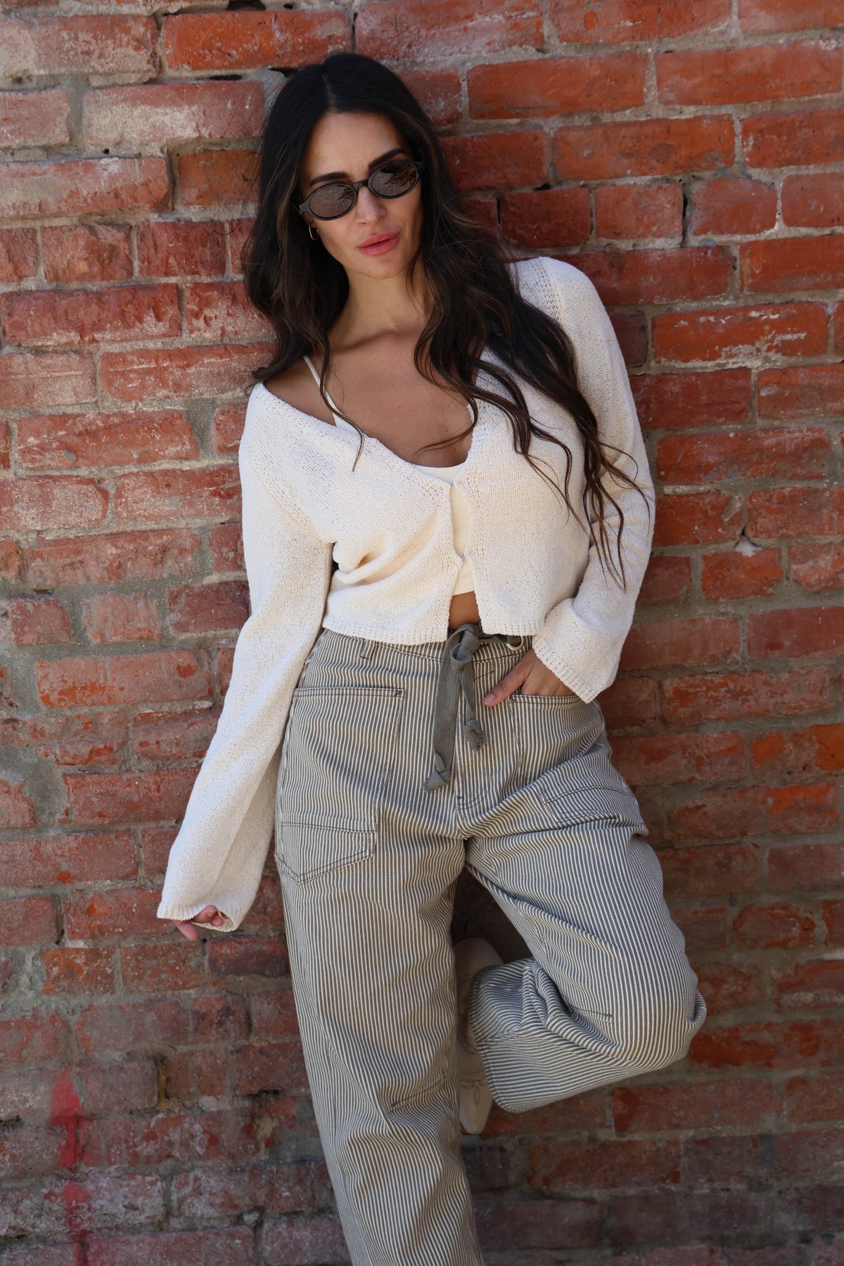 Woman wearing a white knit with striped pants against a brick wall