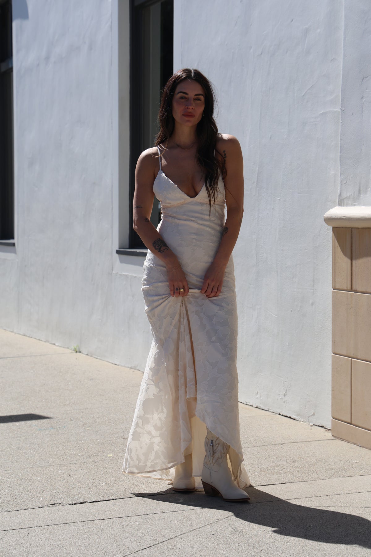 Woman in a white dress standing on a sidewalk with a building in the background