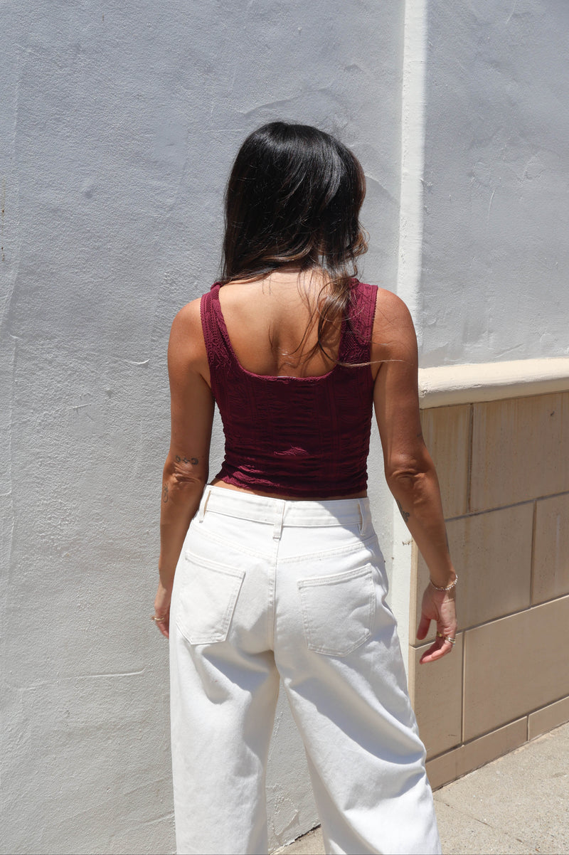 Woman wearing a maroon tank against a white wall