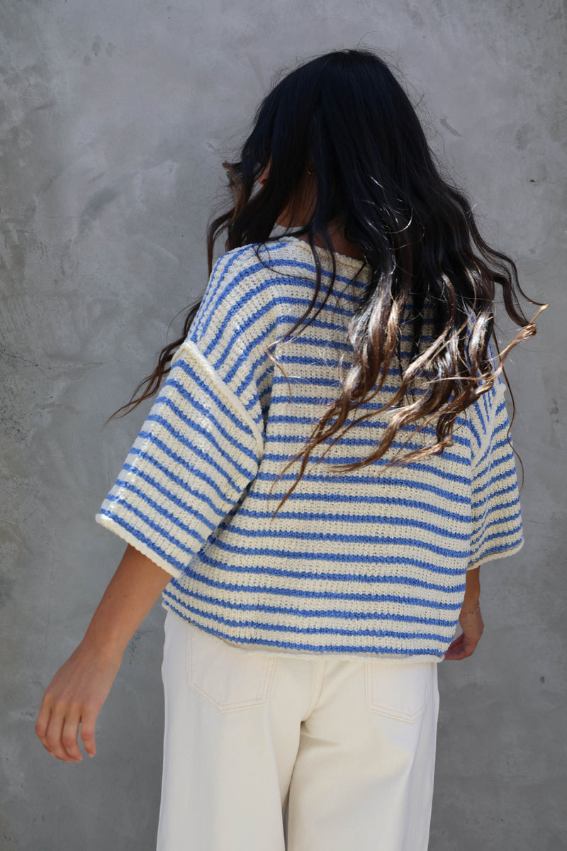 Woman wearing a striped short sleeve knit against a grey wall