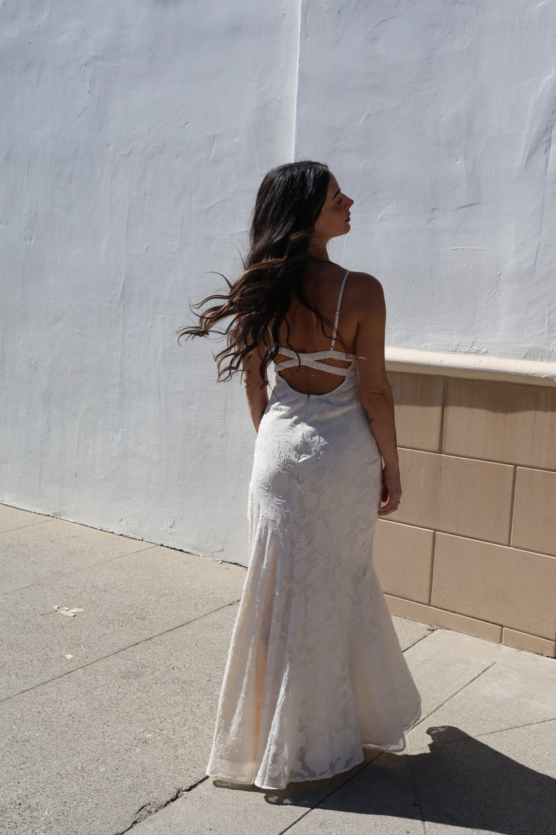 Woman in a white dress standing on a tiled floor with a white wall in the background