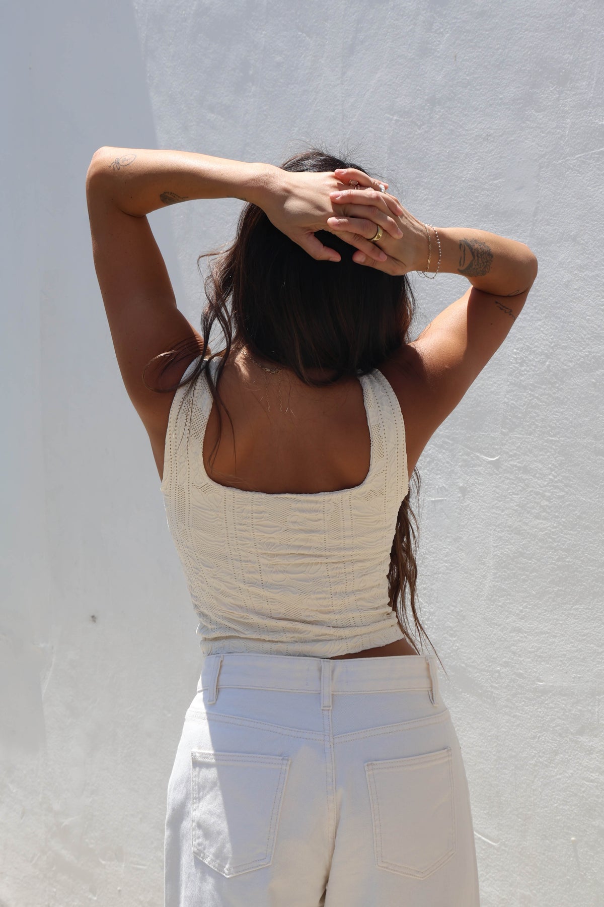 Woman wearing a butter cream tank against a white wall