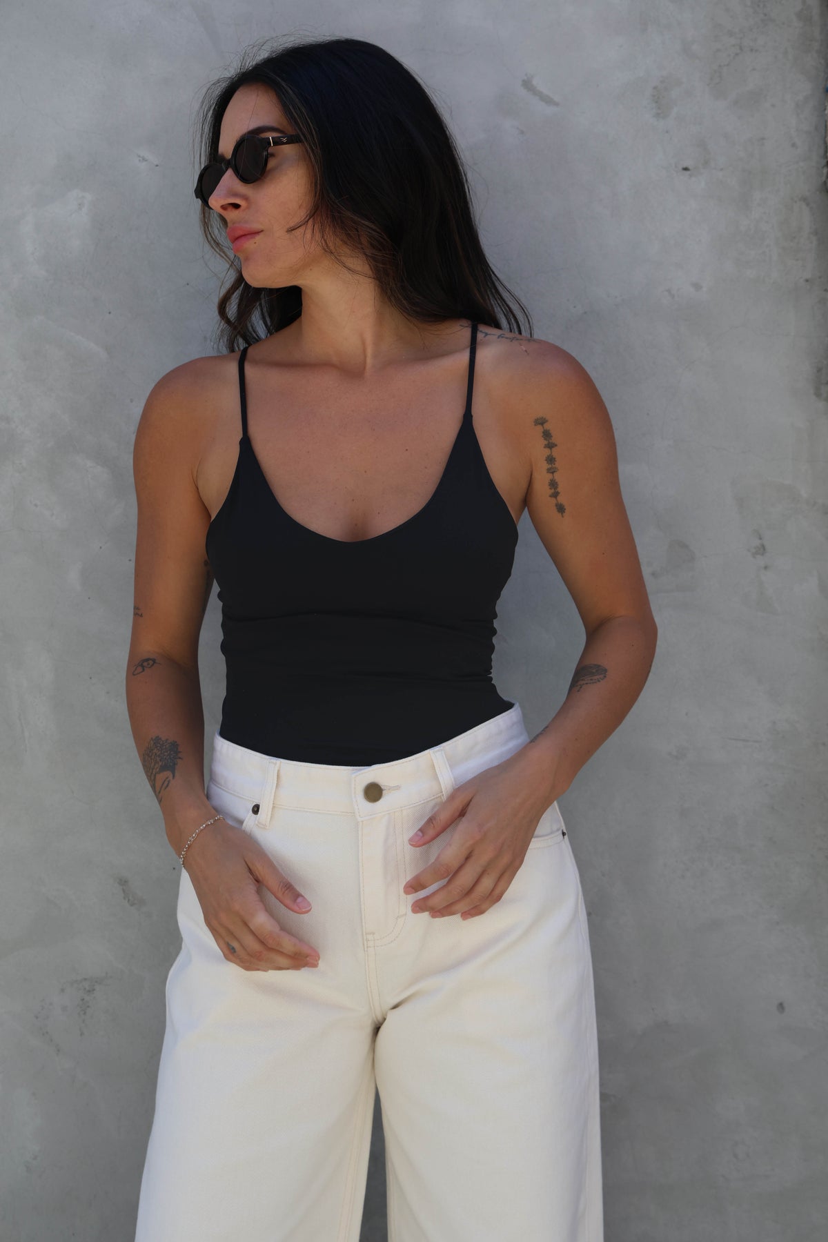 Woman wearing a black tank top and white pants against a gray wall