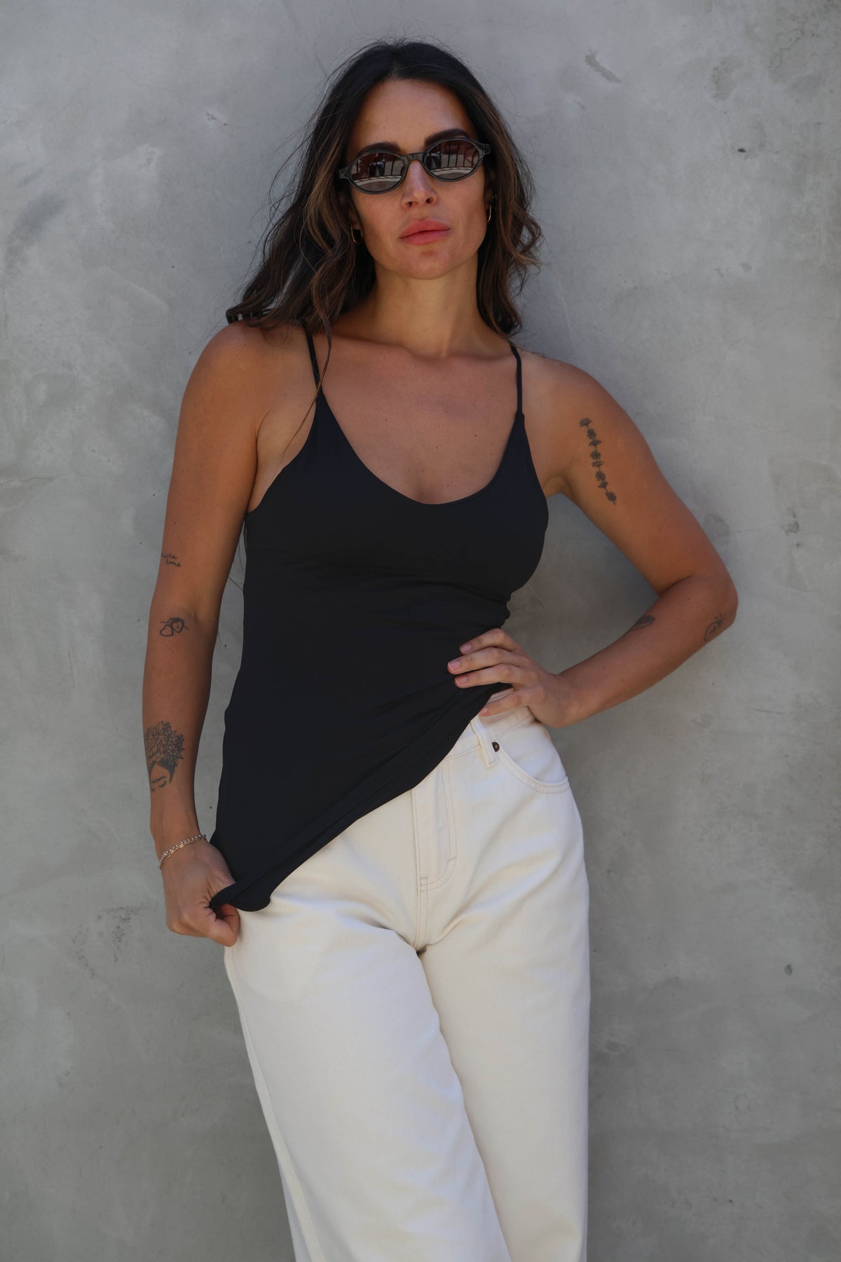 Woman wearing a black tank top and white pants against a gray wall