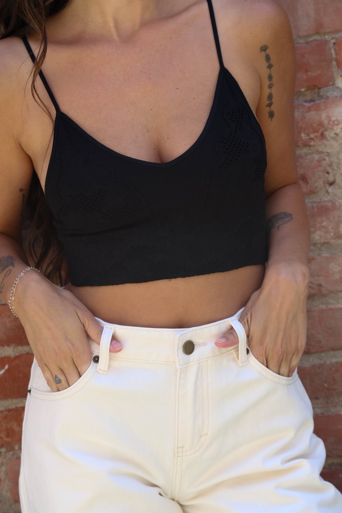 Person wearing a black crop top and white pants against a brick wall.