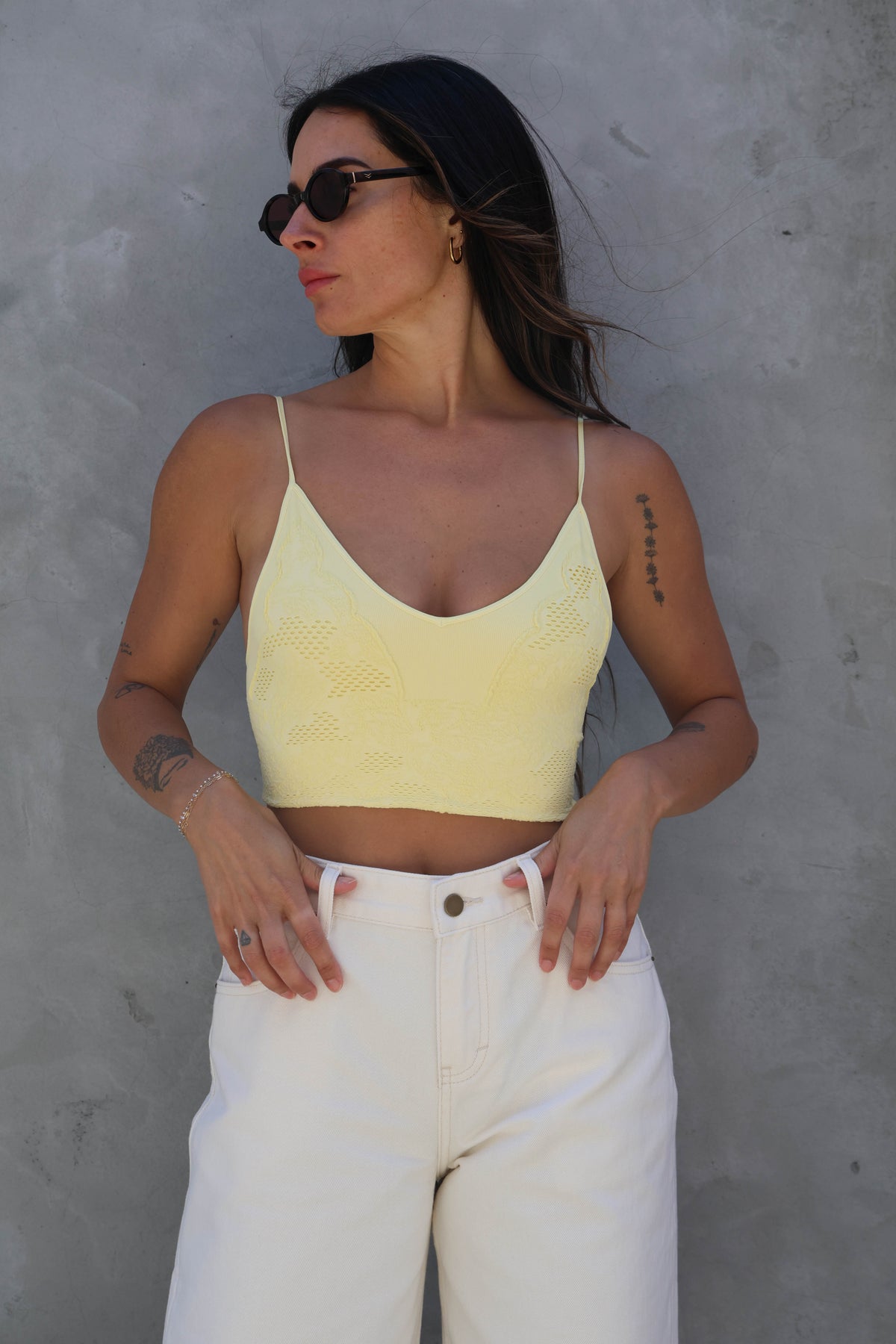 Woman wearing a yellow crop top and white pants against a gray wall