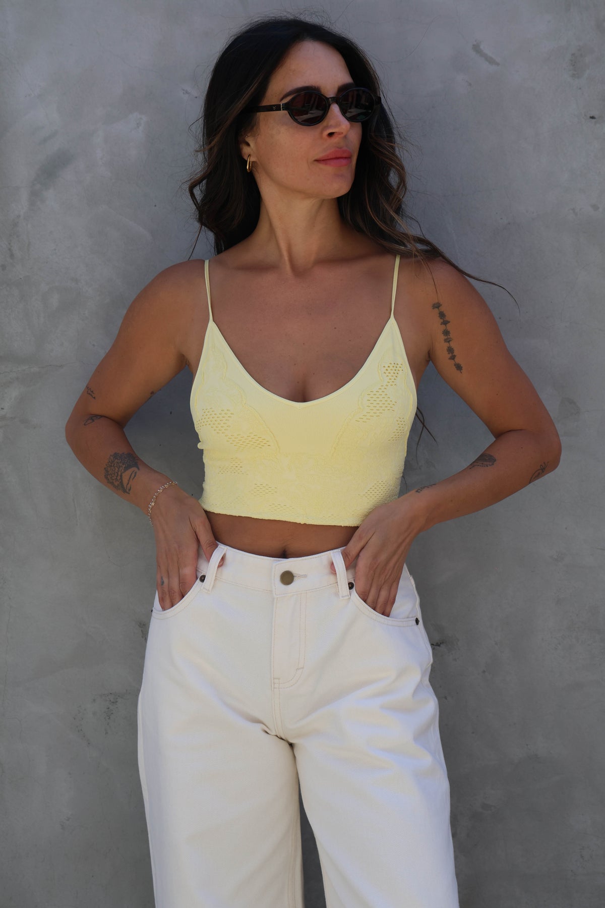 Woman wearing a yellow top and white pants against a gray wall