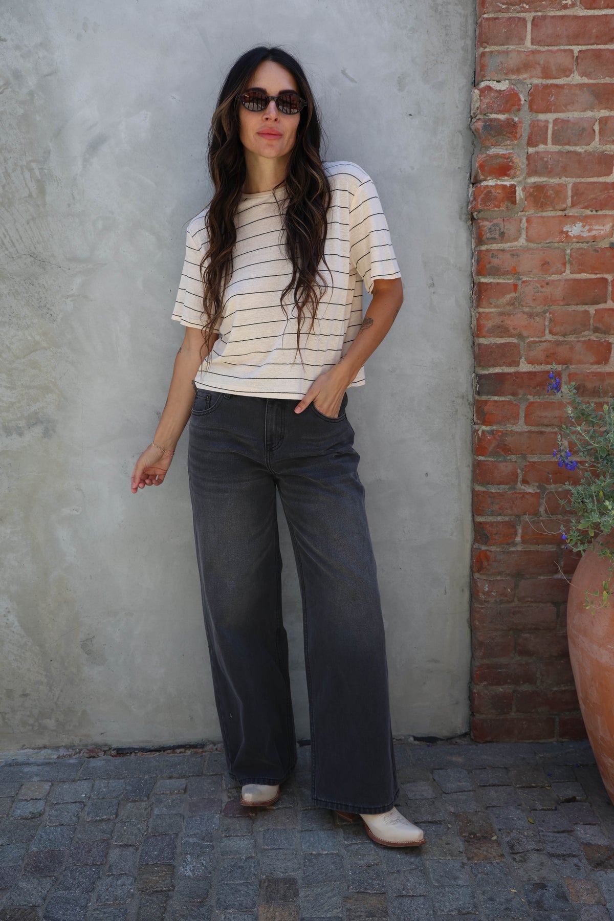 Woman wearing a striped t-shirt with black jeans against a gray wall