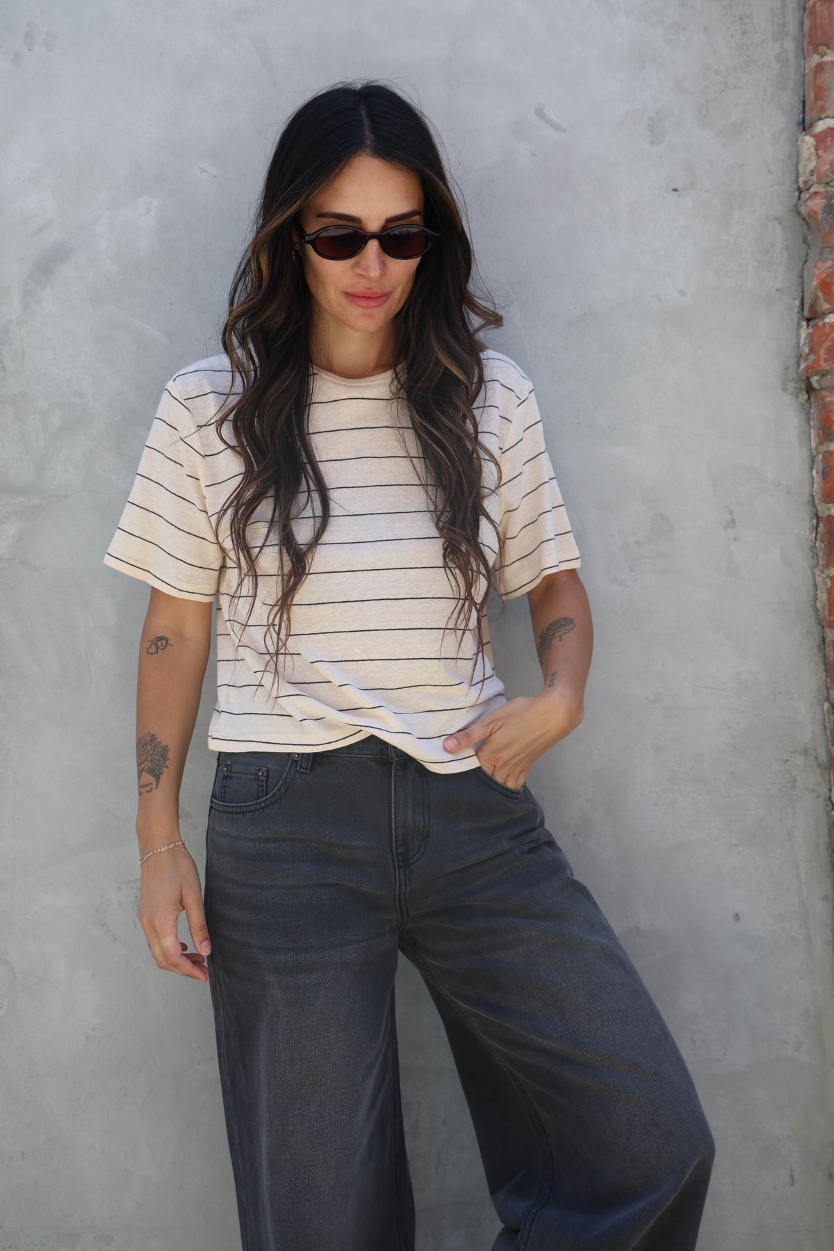 Woman wearing a striped shirt and sunglasses against a gray wall.