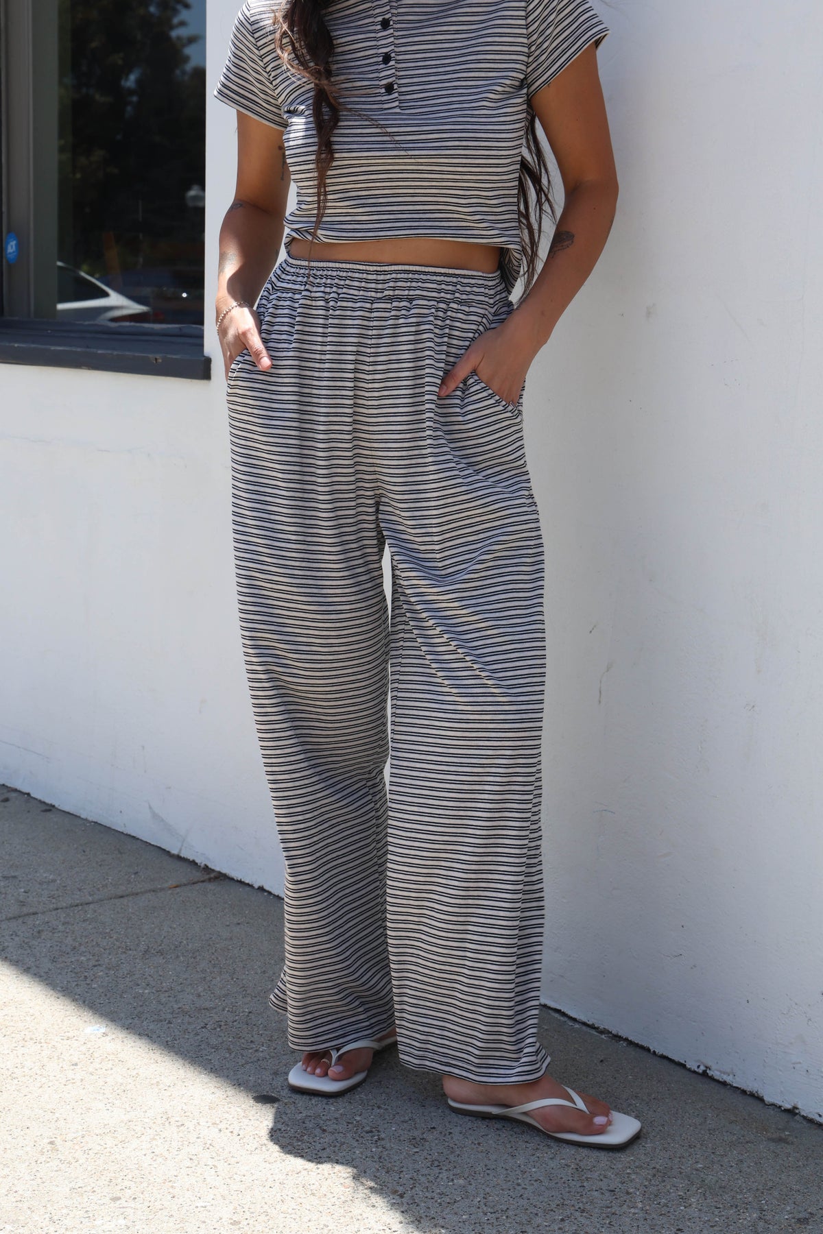 A person wearing a matching striped crop top and wide-leg pants set, standing outdoors against a white wall on a concrete surface.