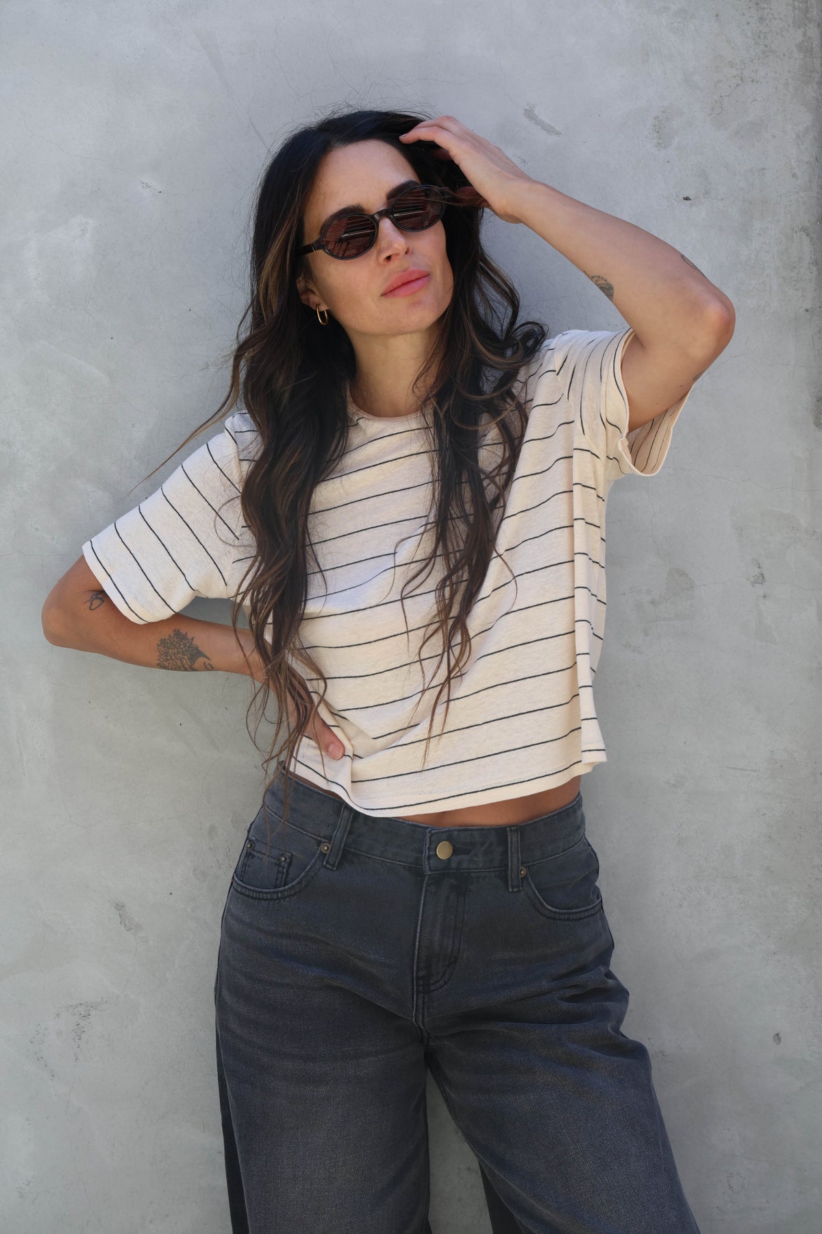Woman wearing a striped t-shirt with black jeans against a gray wall