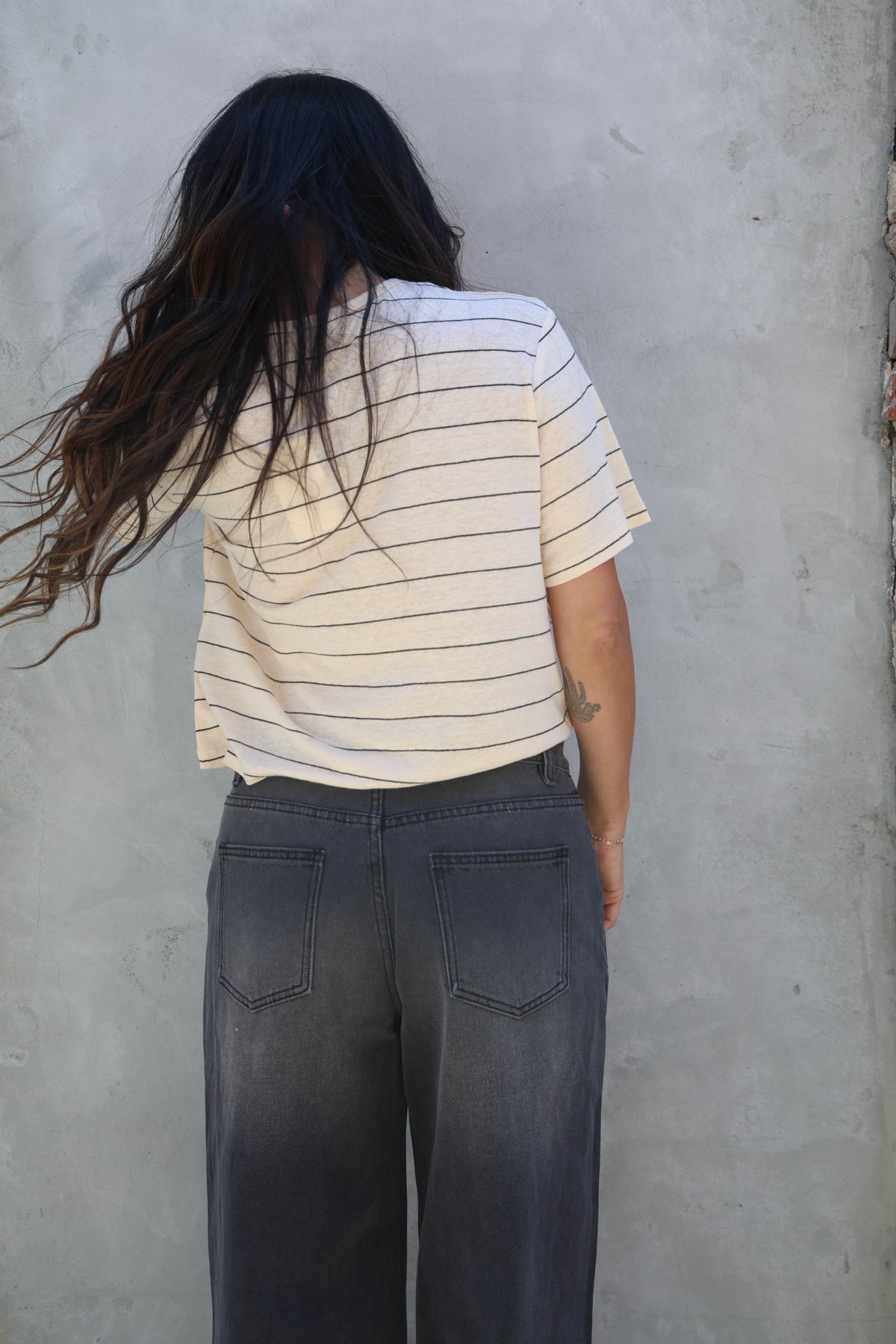 Woman wearing a striped t-shirt with black jeans against a gray wall