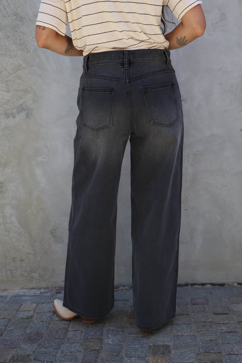 Person wearing dark flared jeans and a striped shirt against a textured wall.