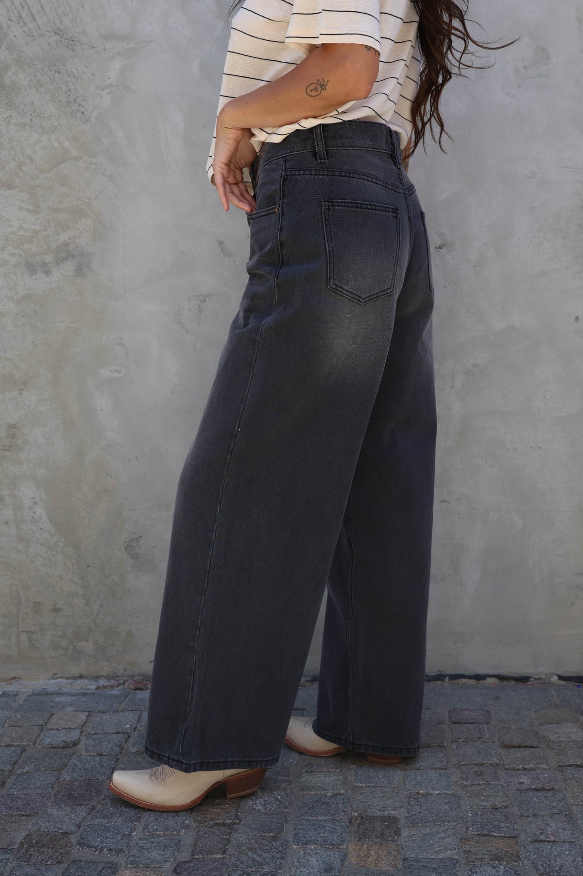 Person wearing dark wide-leg jeans and a striped shirt against a textured wall.
