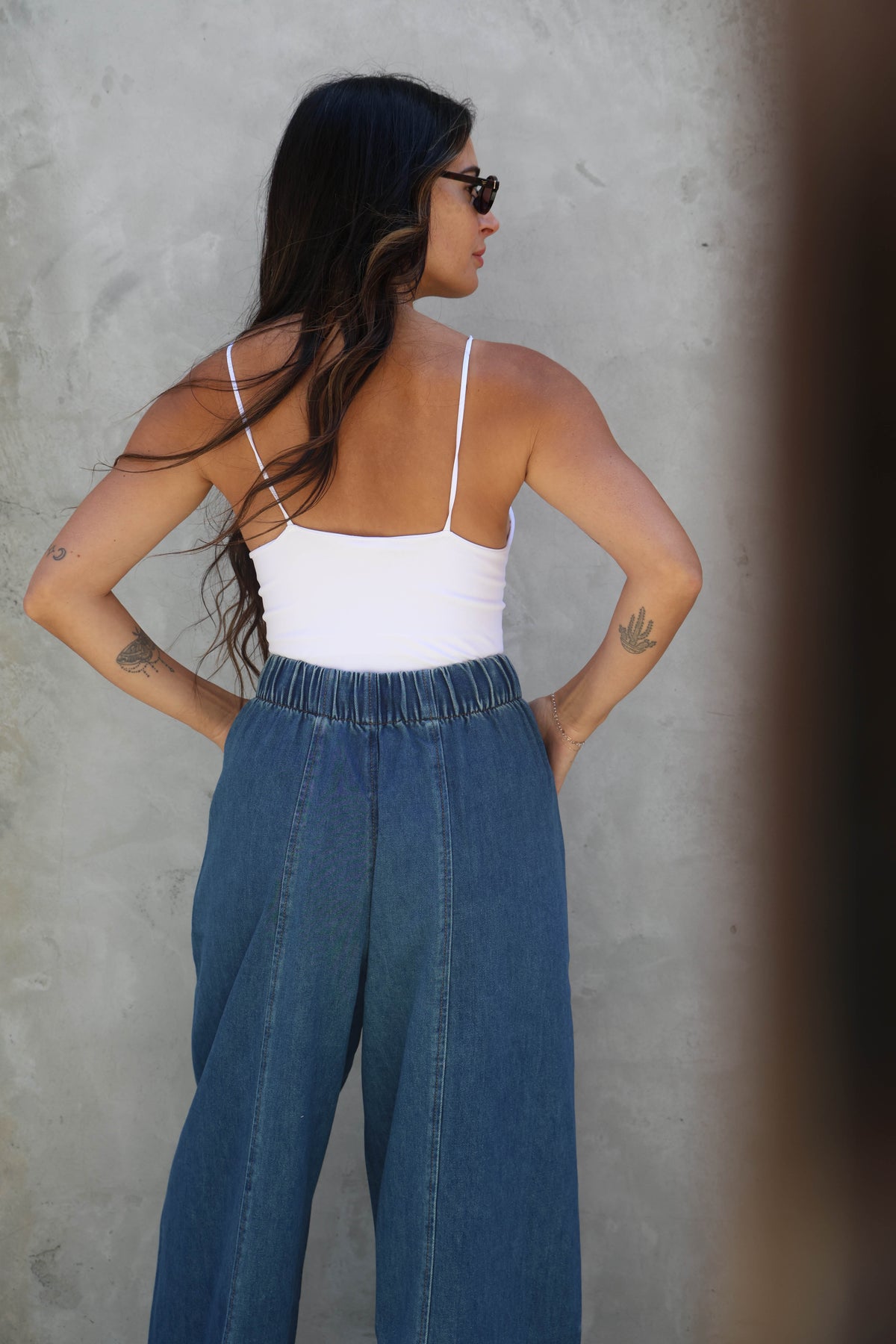 Woman wearing a white top and blue jeans against a gray wall