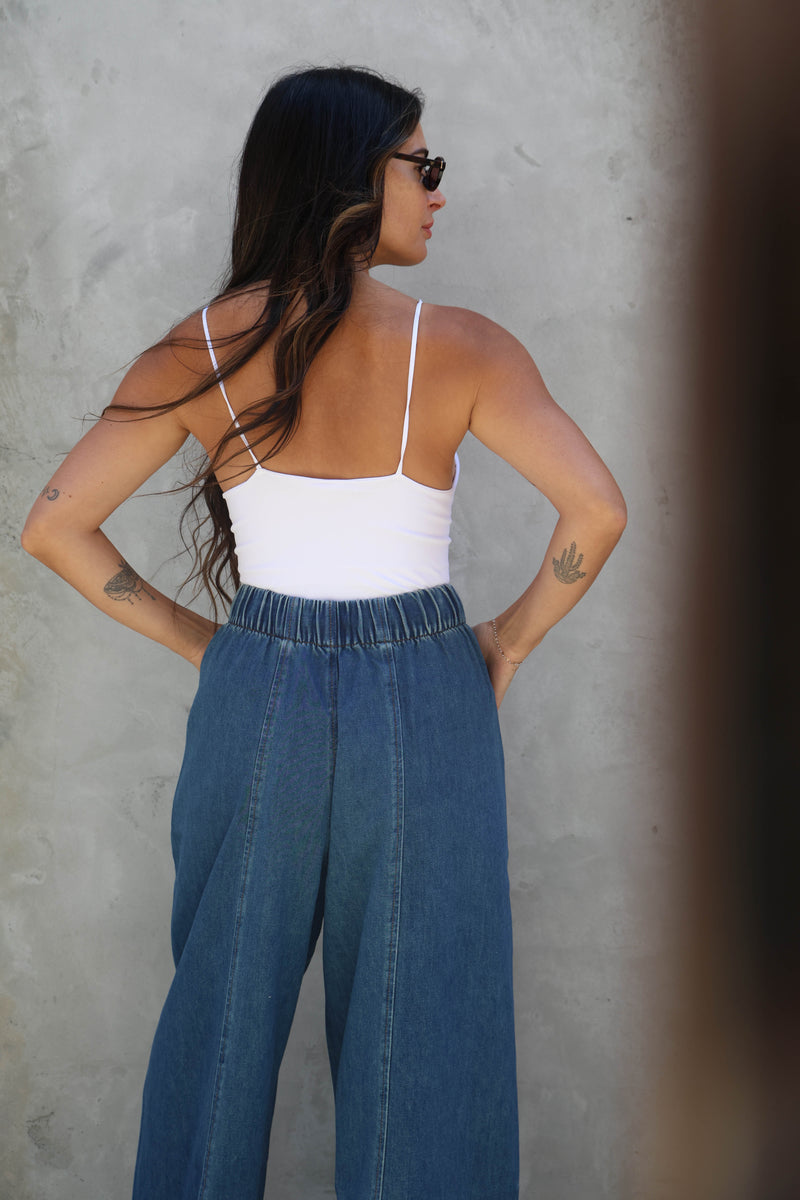 Woman wearing a white top and blue jeans against a gray wall