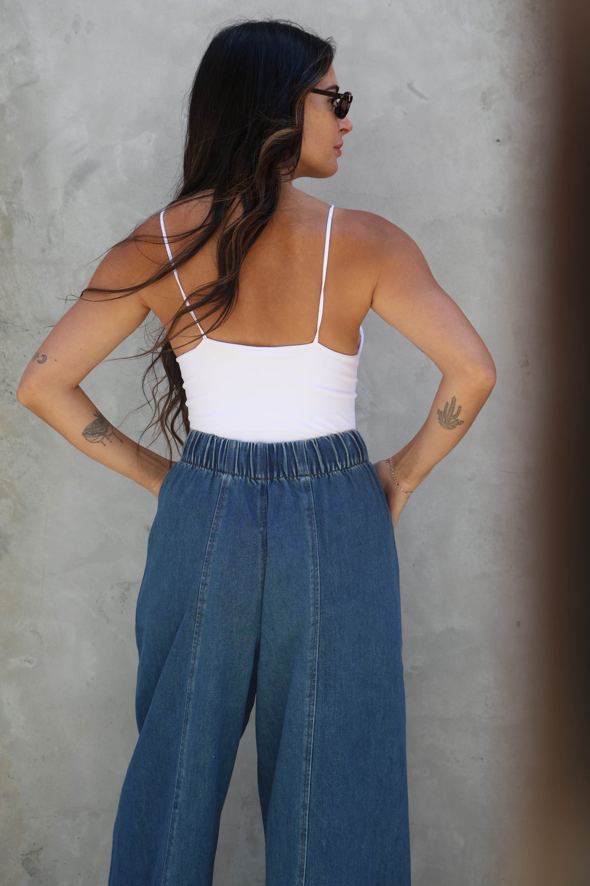 Woman wearing a white top and blue jeans against a gray wall