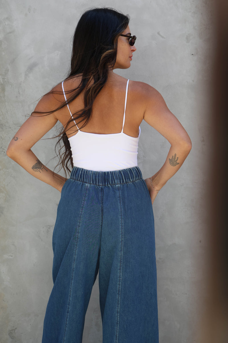 Woman wearing a white top and blue jeans against a gray wall